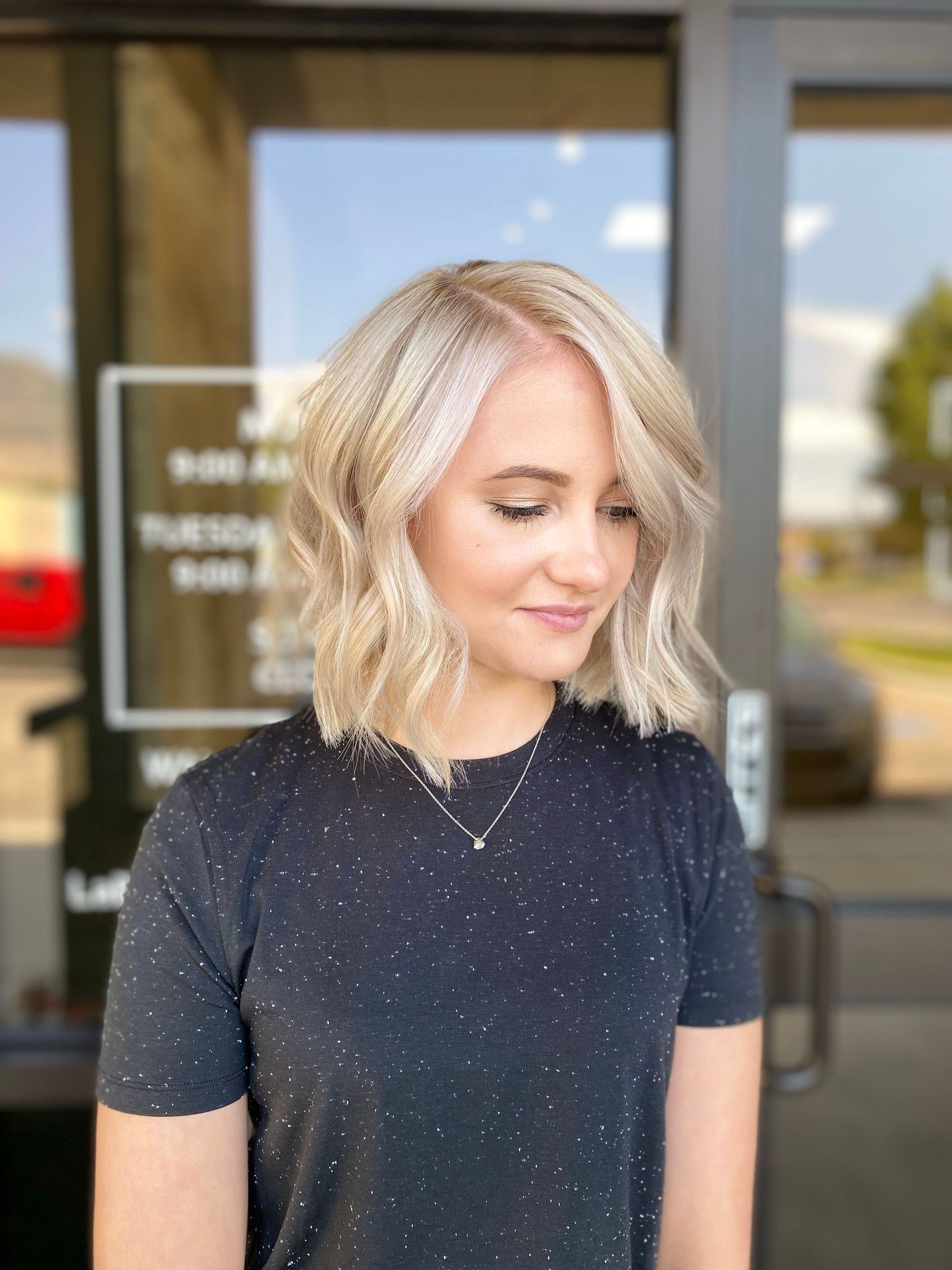 A woman with blonde hair and a black shirt is standing in front of a building.