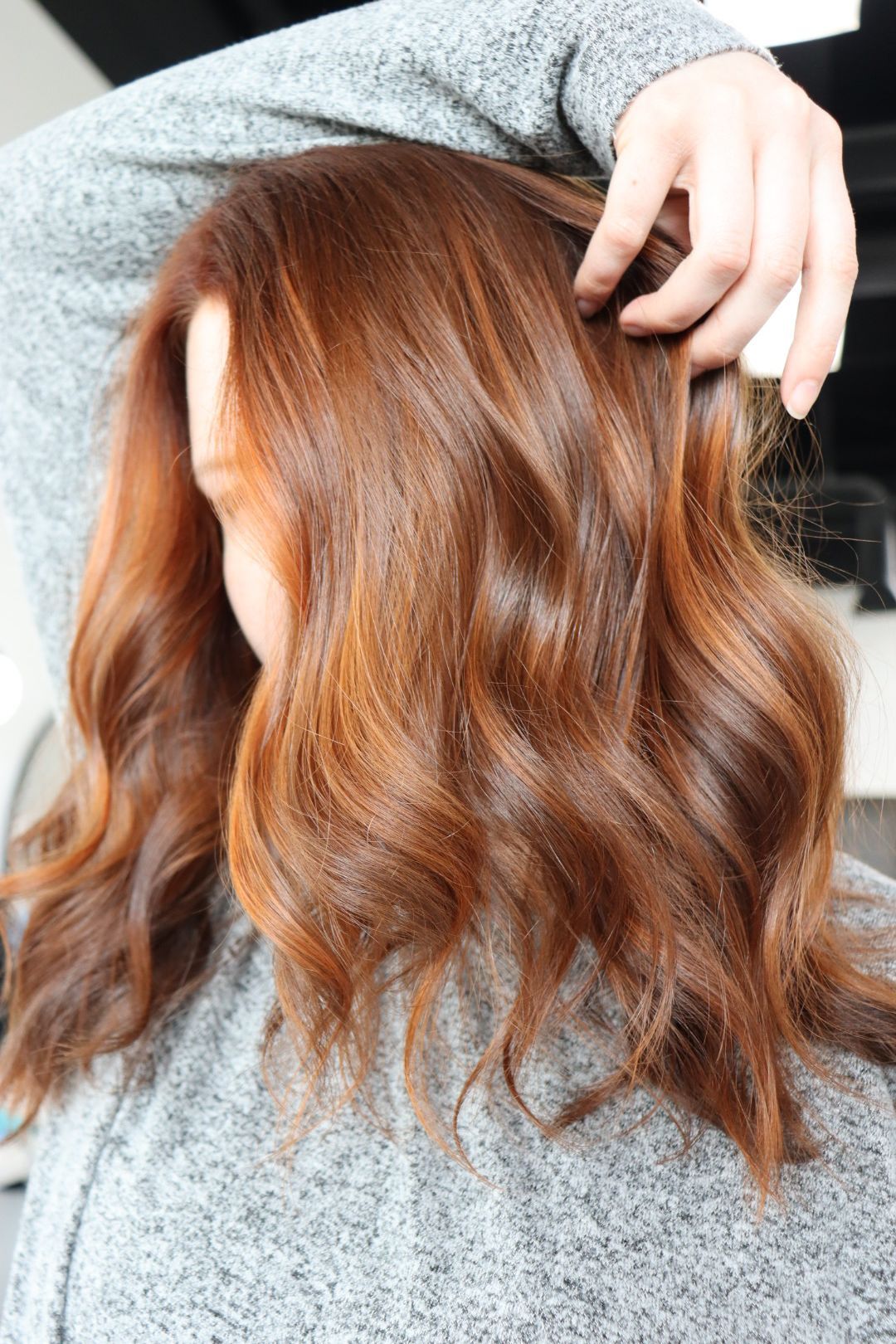 A woman with long brown hair is wearing a grey sweater.