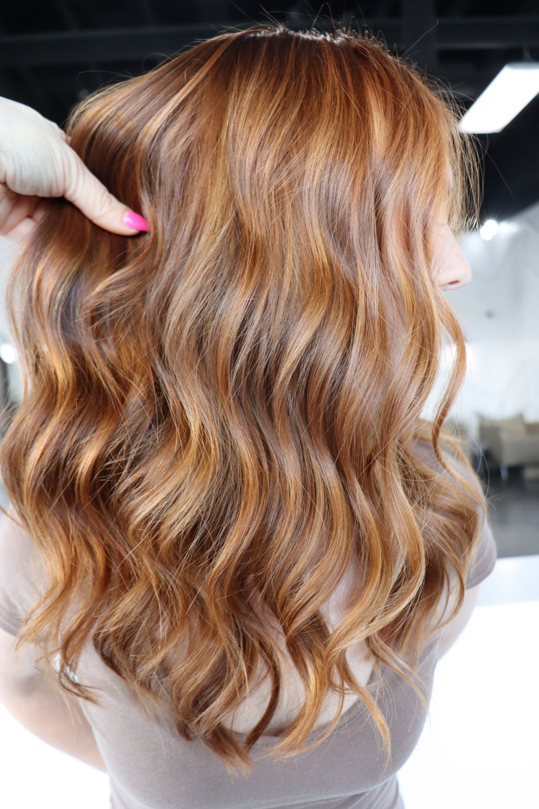 A woman with long wavy red hair is getting her hair done by a hairdresser.