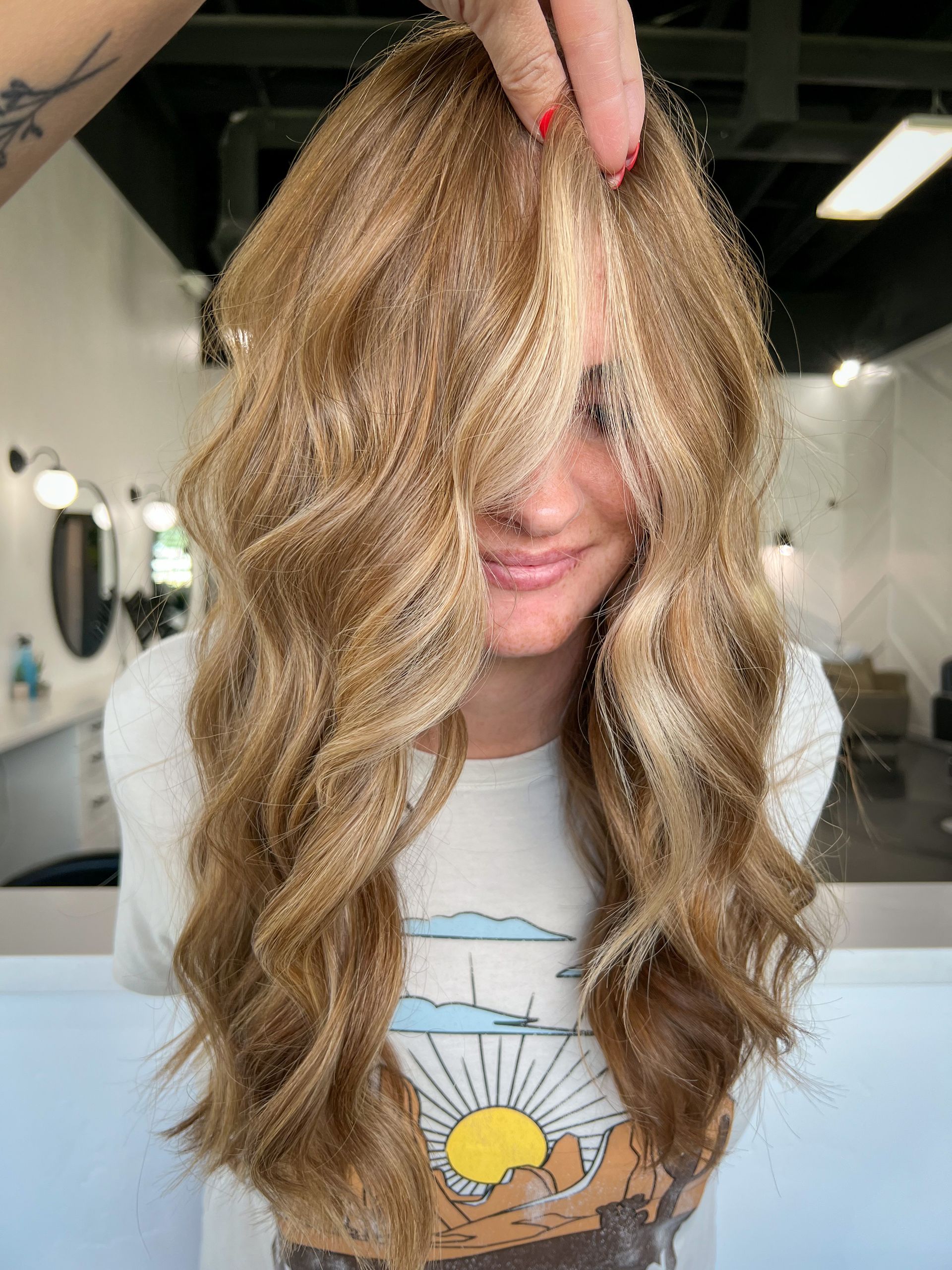 A woman with long blonde hair is covering her face with her hair.