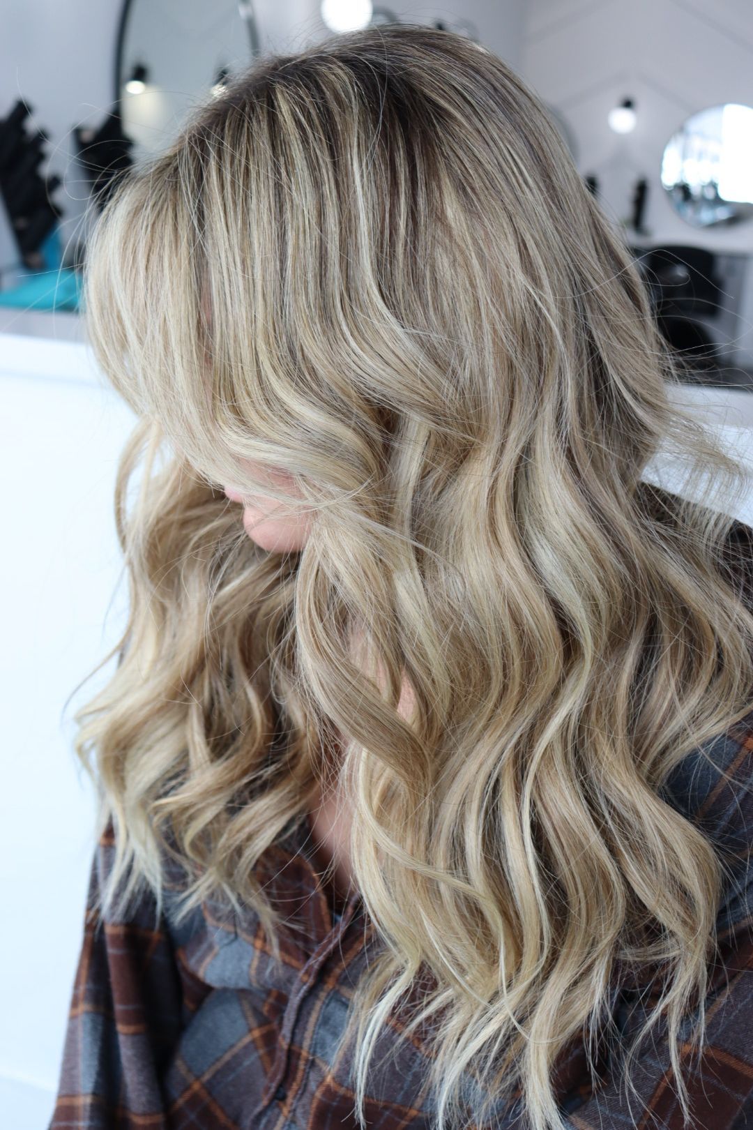 A woman with long blonde wavy hair is wearing a plaid shirt.