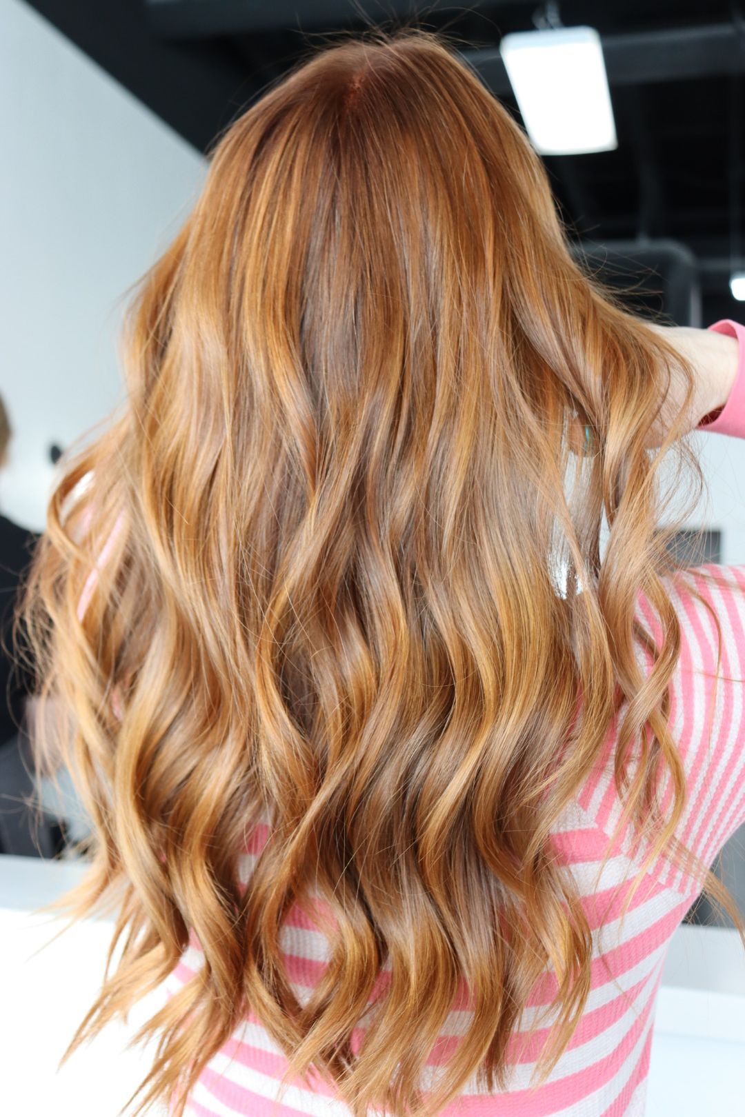 A woman with long red hair is wearing a pink and white striped shirt.