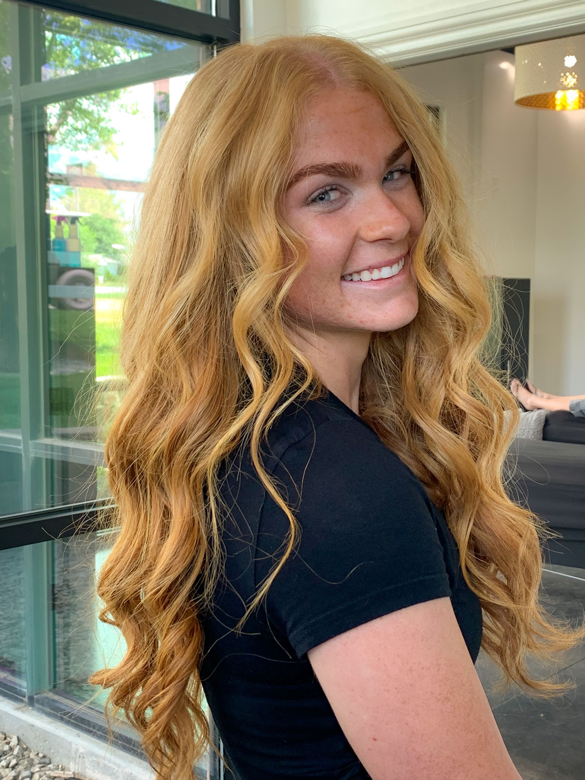 A woman with long blonde hair is wearing a black shirt and smiling.