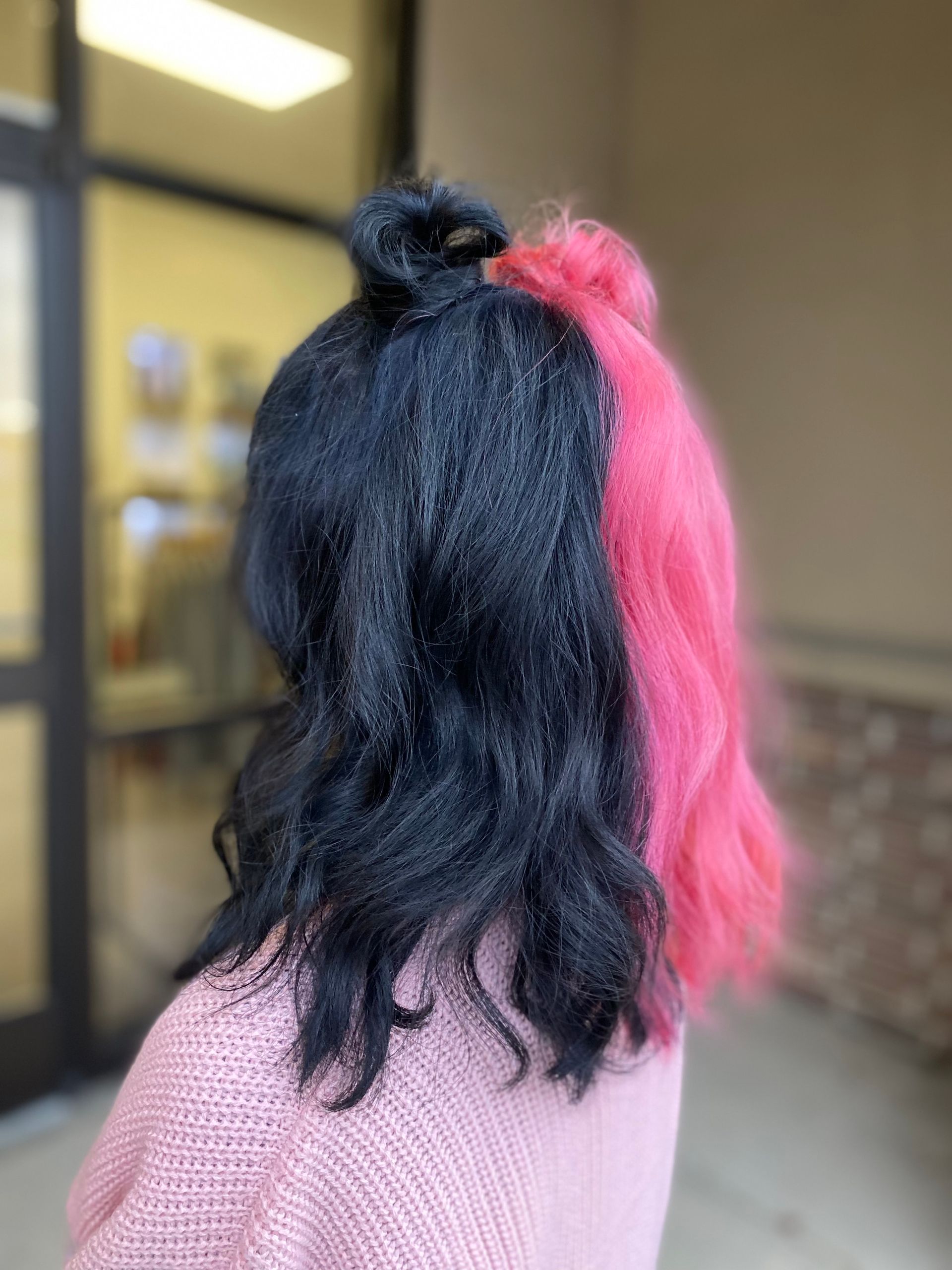 A woman with black and pink hair is wearing a pink sweater.