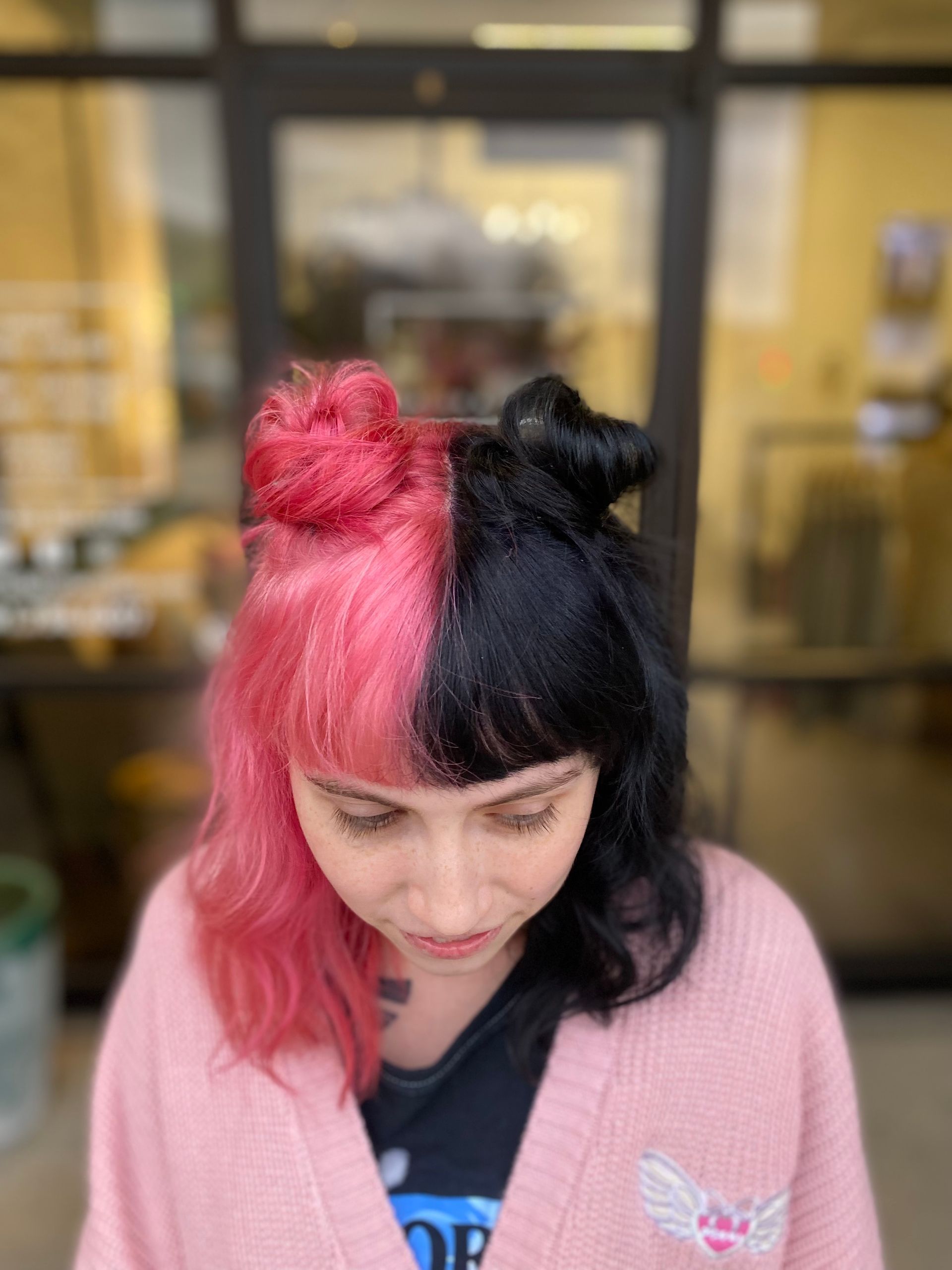A woman with pink and black hair is wearing a pink sweater.
