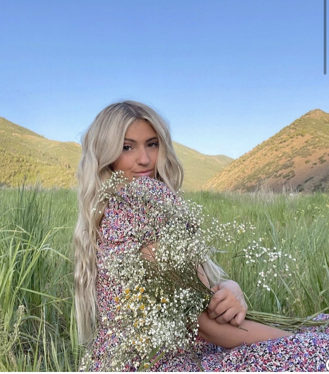 A woman is sitting in a field holding a bouquet of baby 's breath flowers.