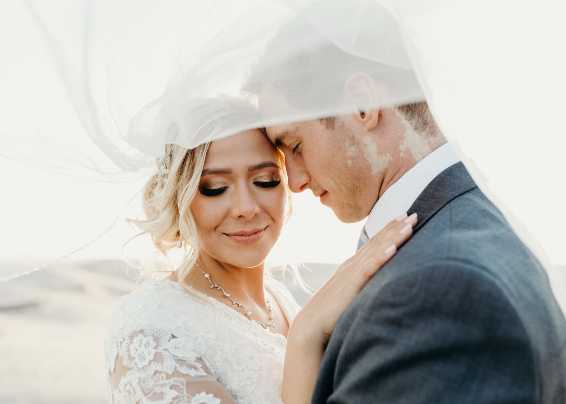 A bride and groom are posing for a picture under a veil.