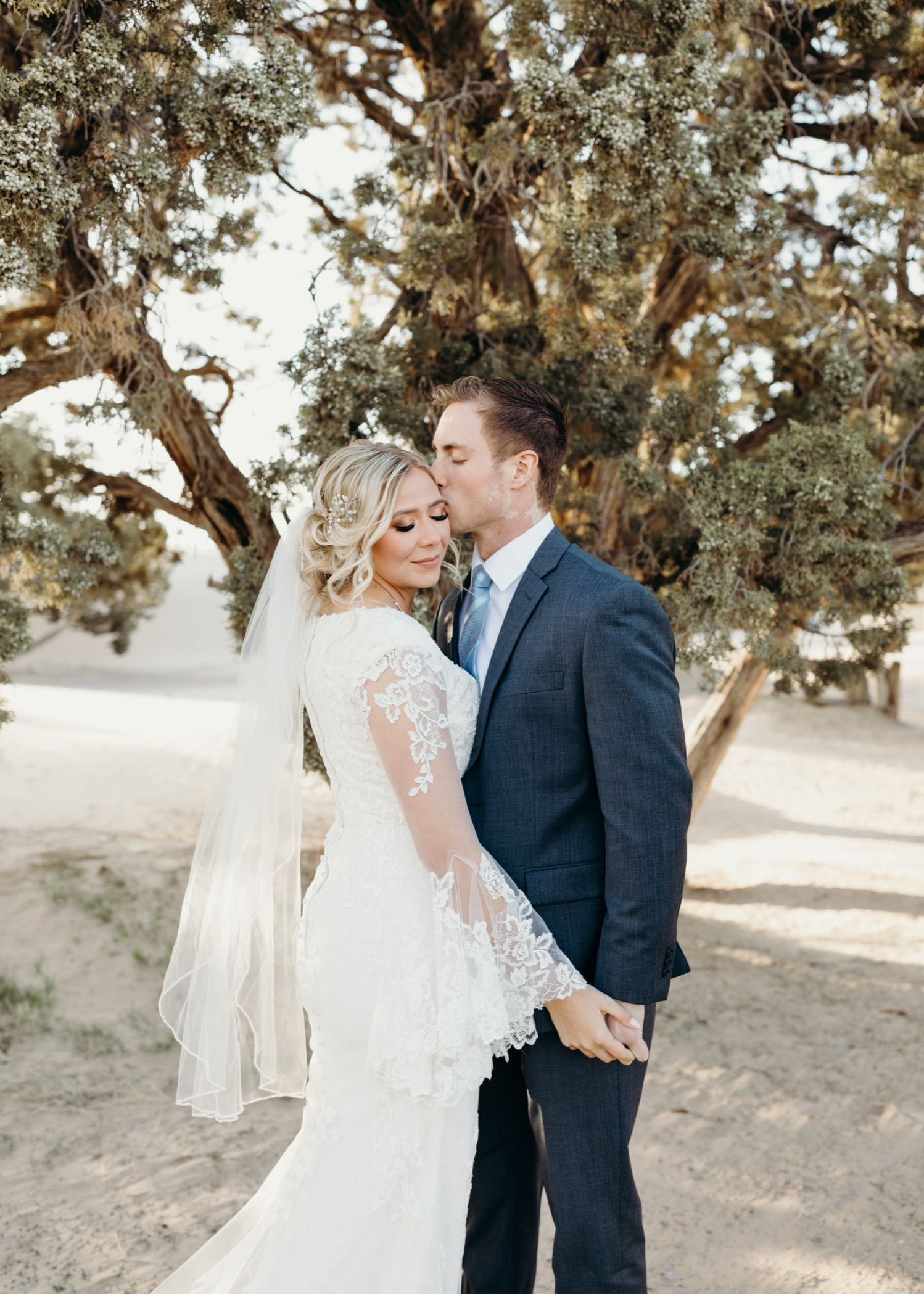 A bride and groom are kissing in front of a tree.