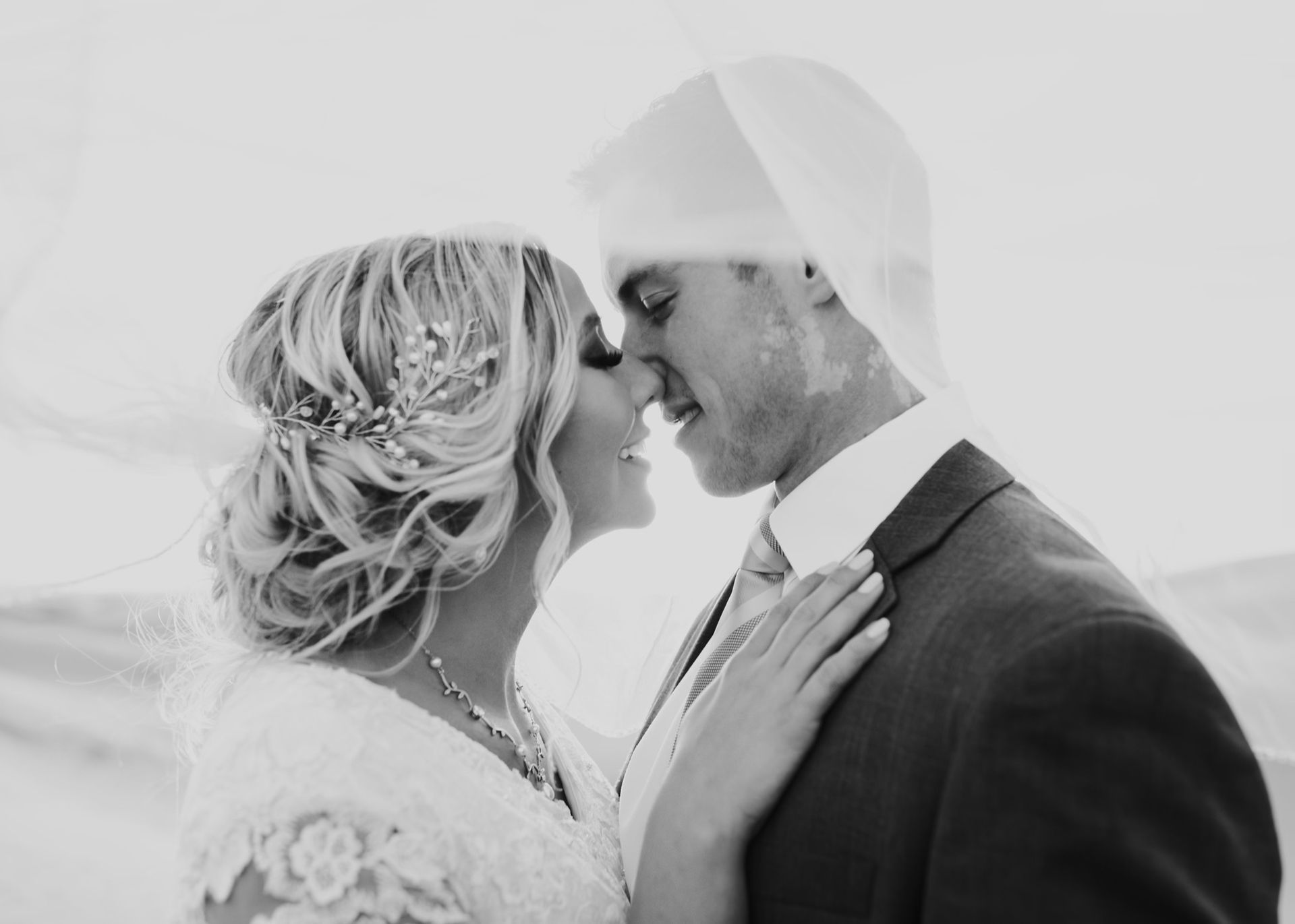 A bride and groom are kissing under a veil in a black and white photo.