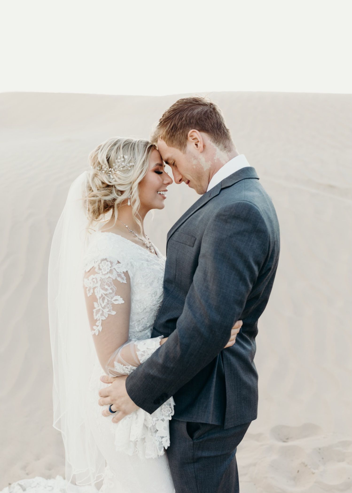 A bride and groom are standing next to each other on a sandy beach.