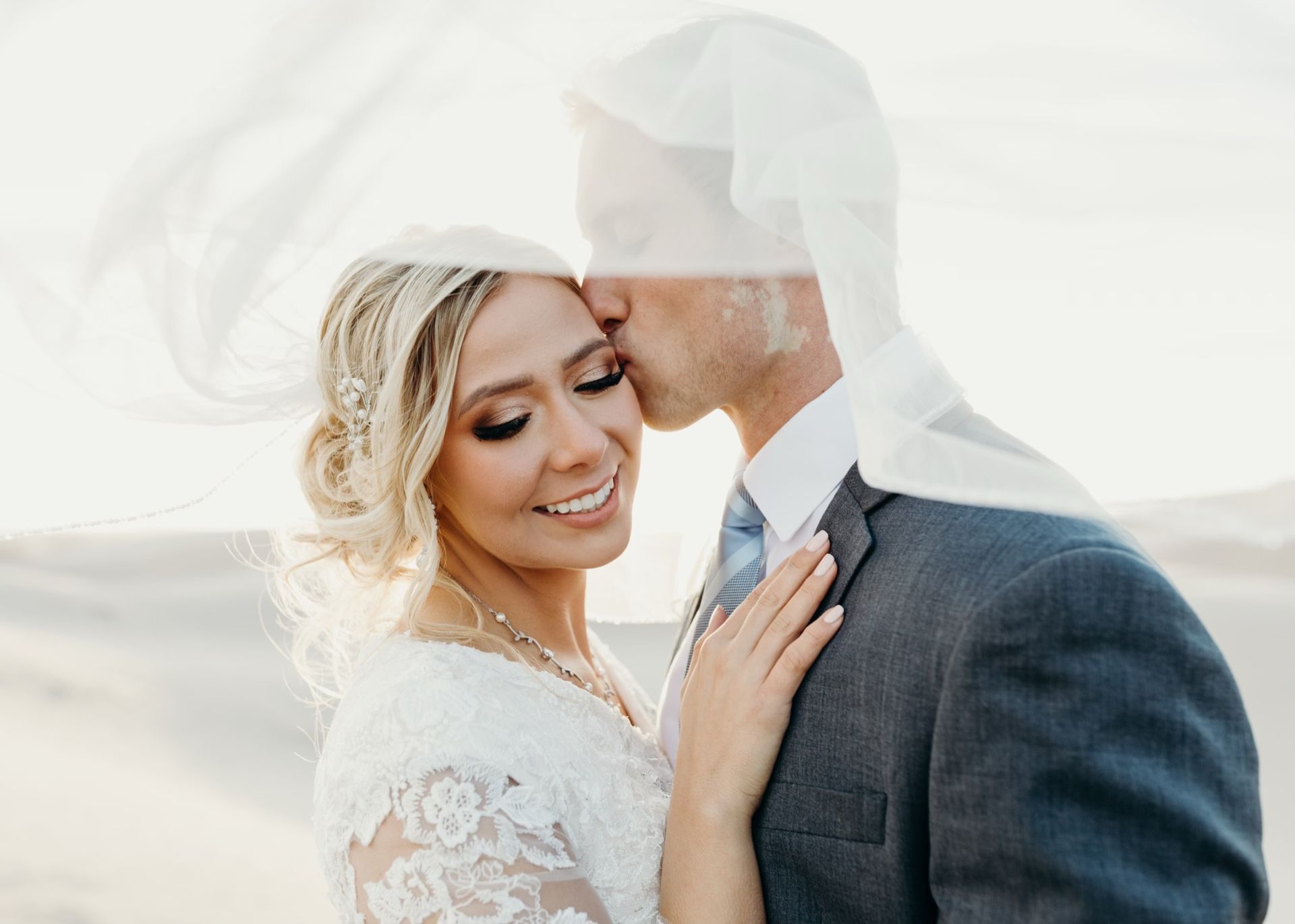 A bride and groom are kissing under a veil.