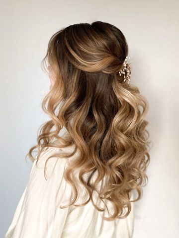A woman with long wavy hair is wearing a half up half down hairstyle.