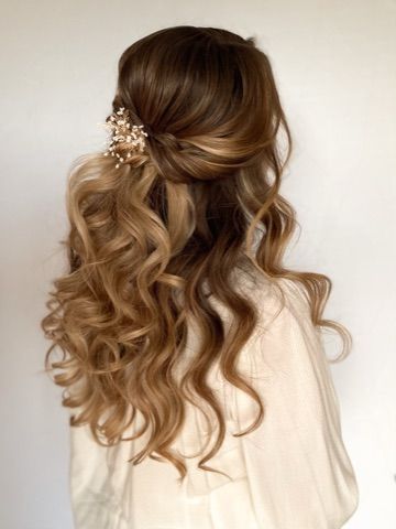 A woman with long hair is wearing a half up half down hairstyle with a flower in her hair.