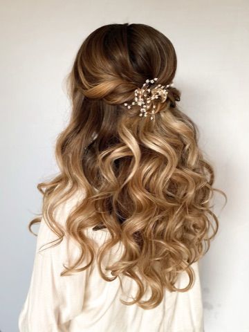 A woman with long curly hair is wearing a half up half down hairstyle.