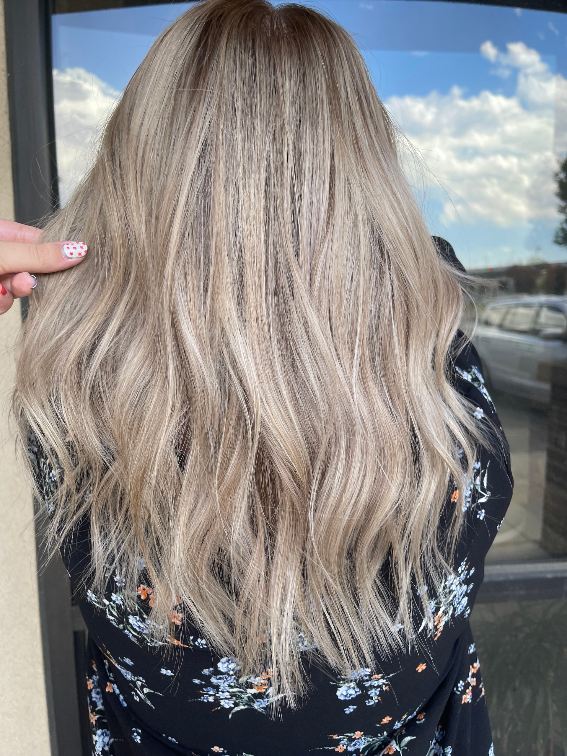 A woman with long blonde hair is standing in front of a window.