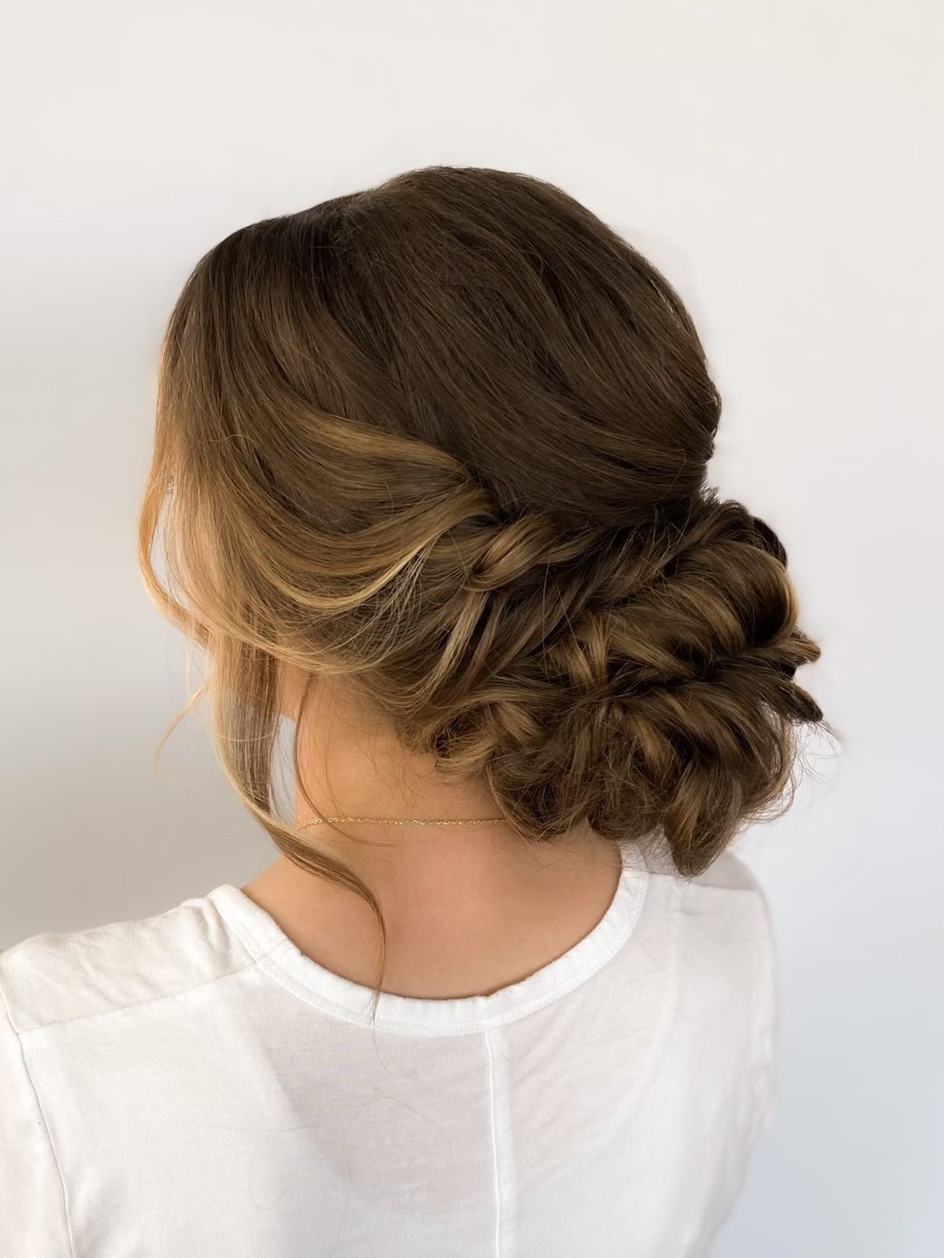 Woman with brown hair styled in an updo, with loose strands framing the face, against a white background.