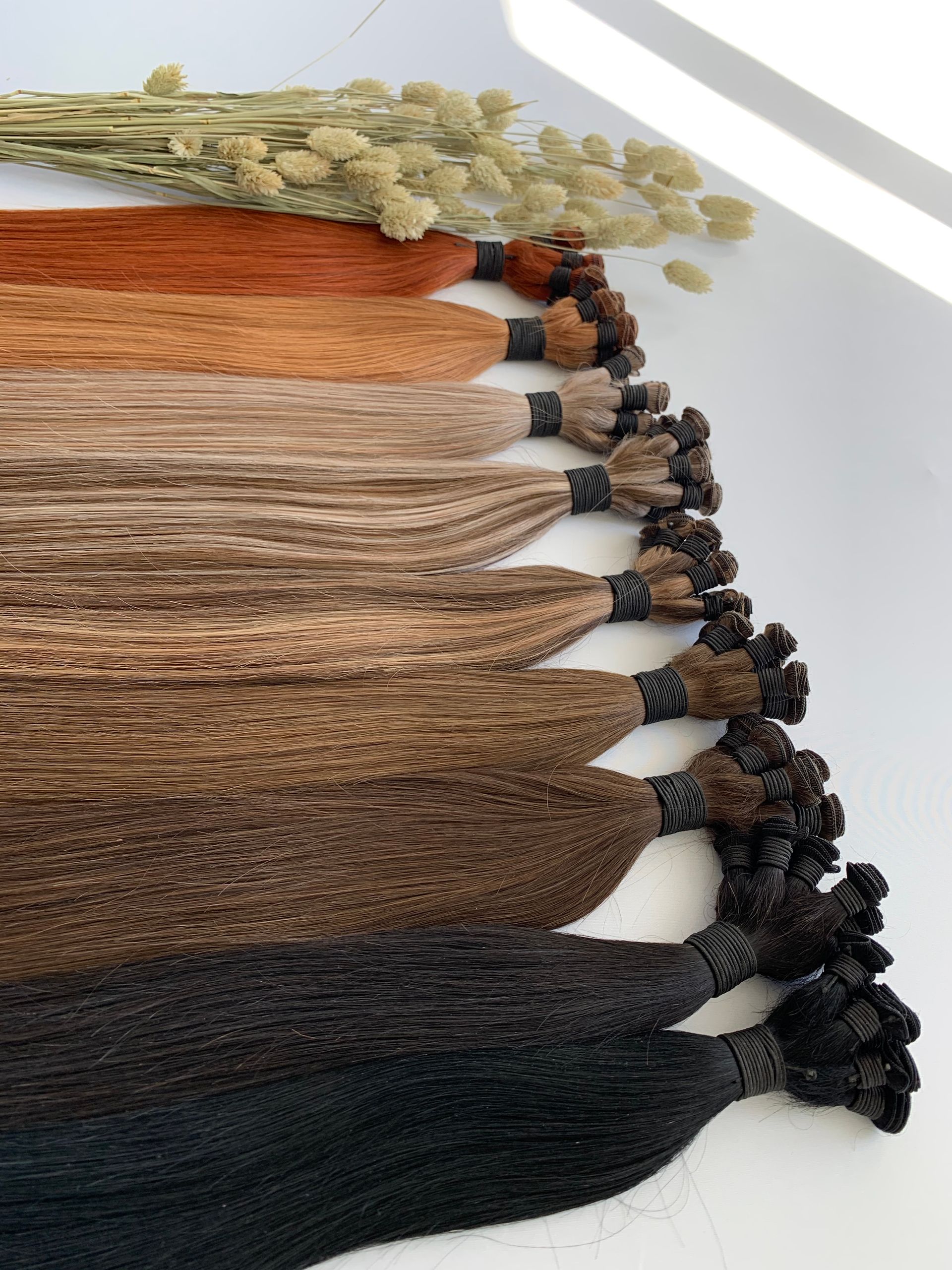 Hair extensions in various shades of brown and black, displayed in a row on a white surface.