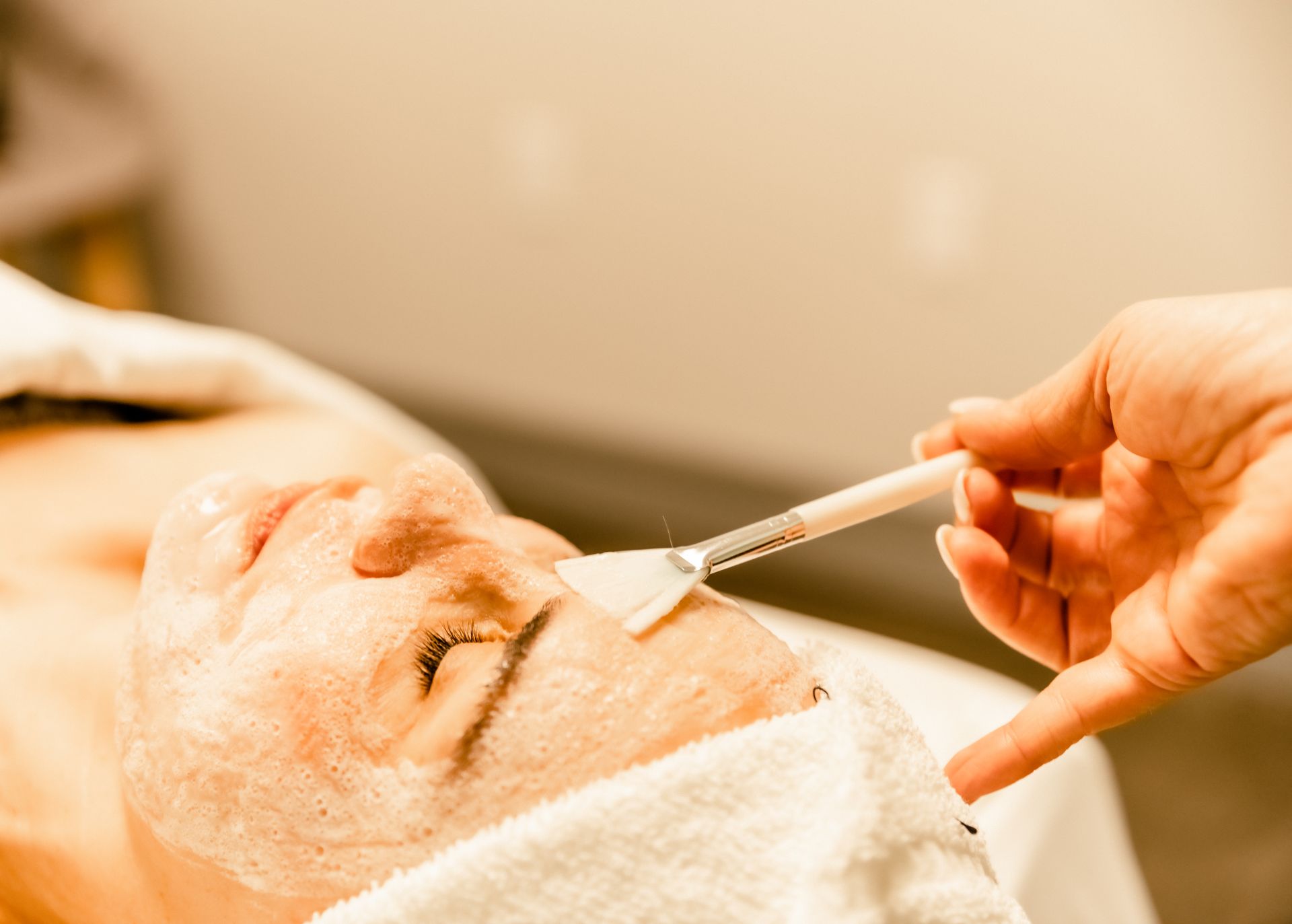 Person receiving facial treatment; hand applying product with brush.
