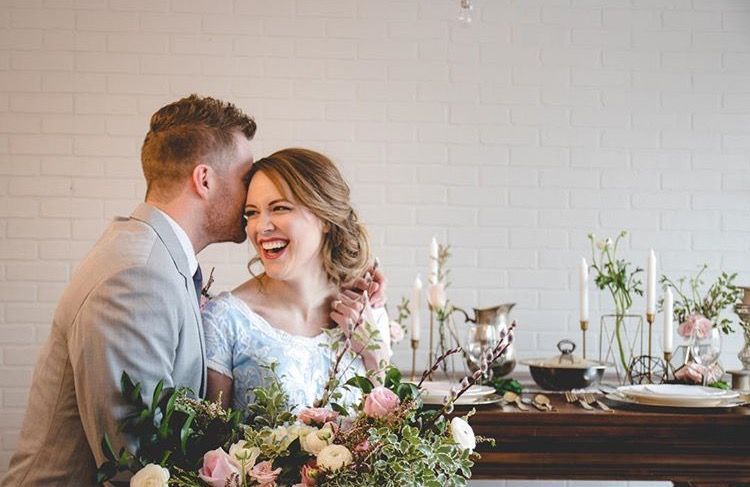 Bride laughs as groom kisses her cheek; wedding decor on table.