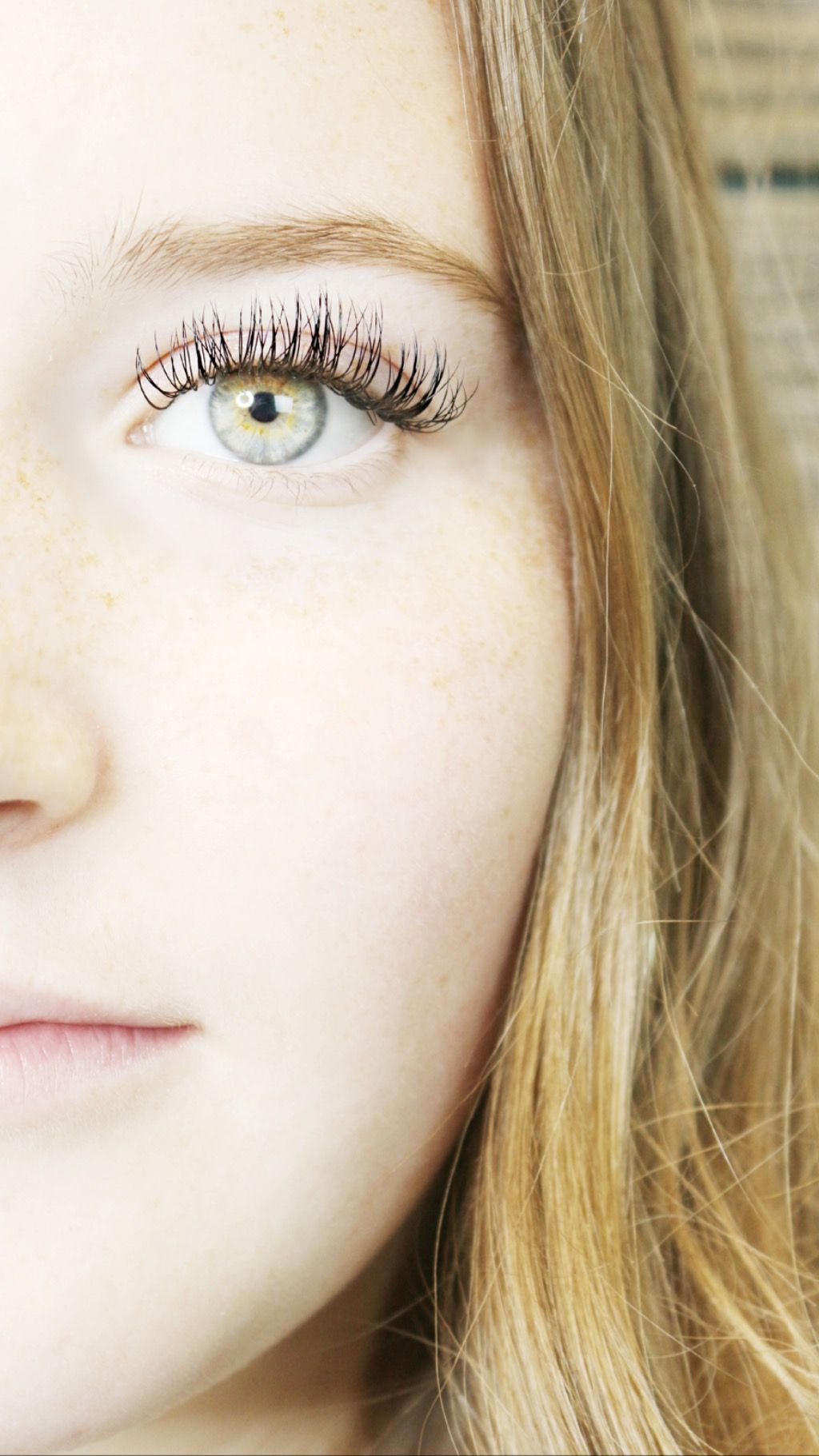 Close-up of a person's face: light skin, blue-green eye with long lashes, blonde hair, soft expression.