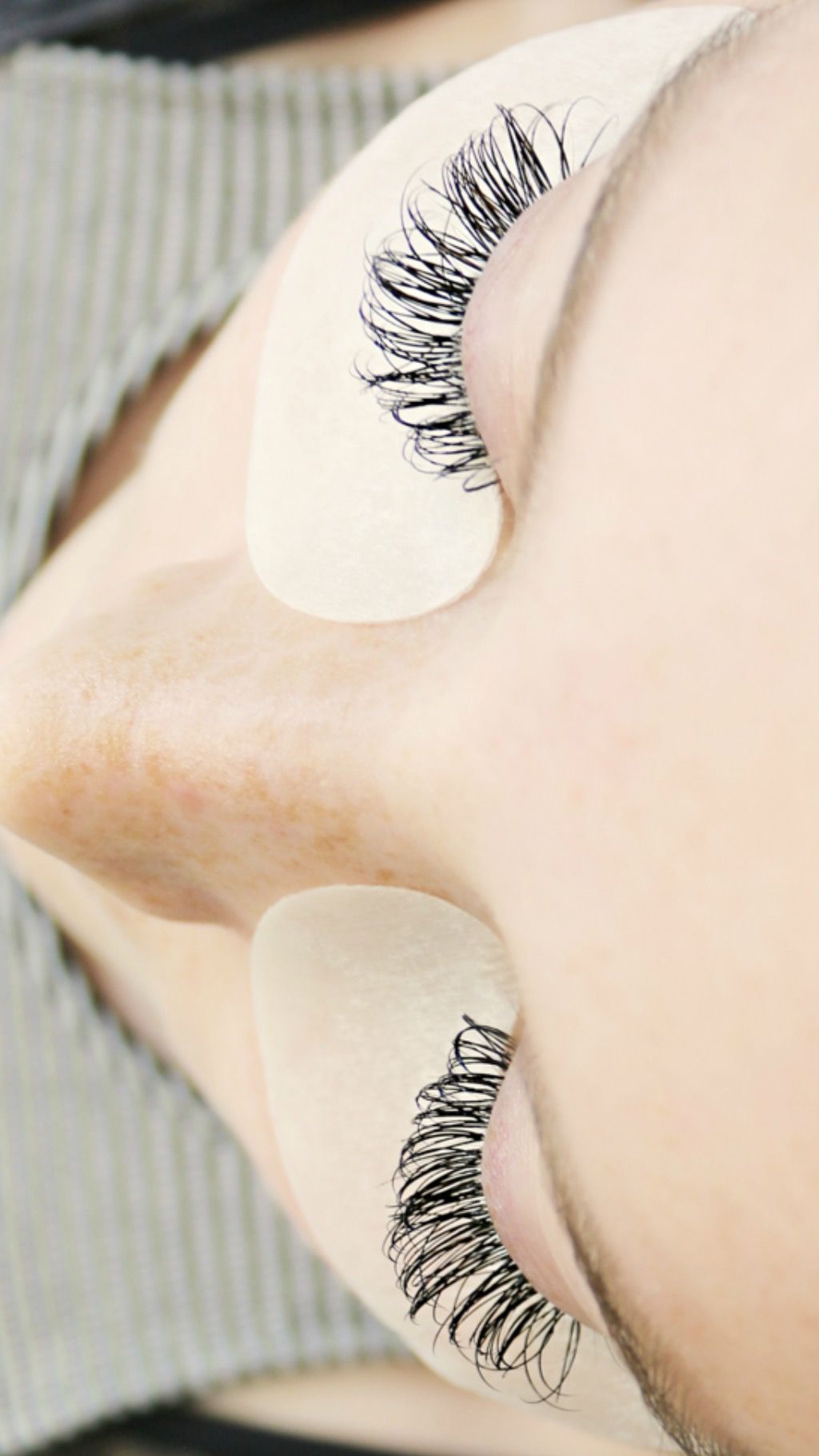 Person with extended eyelashes, eye pads in place, angled view.