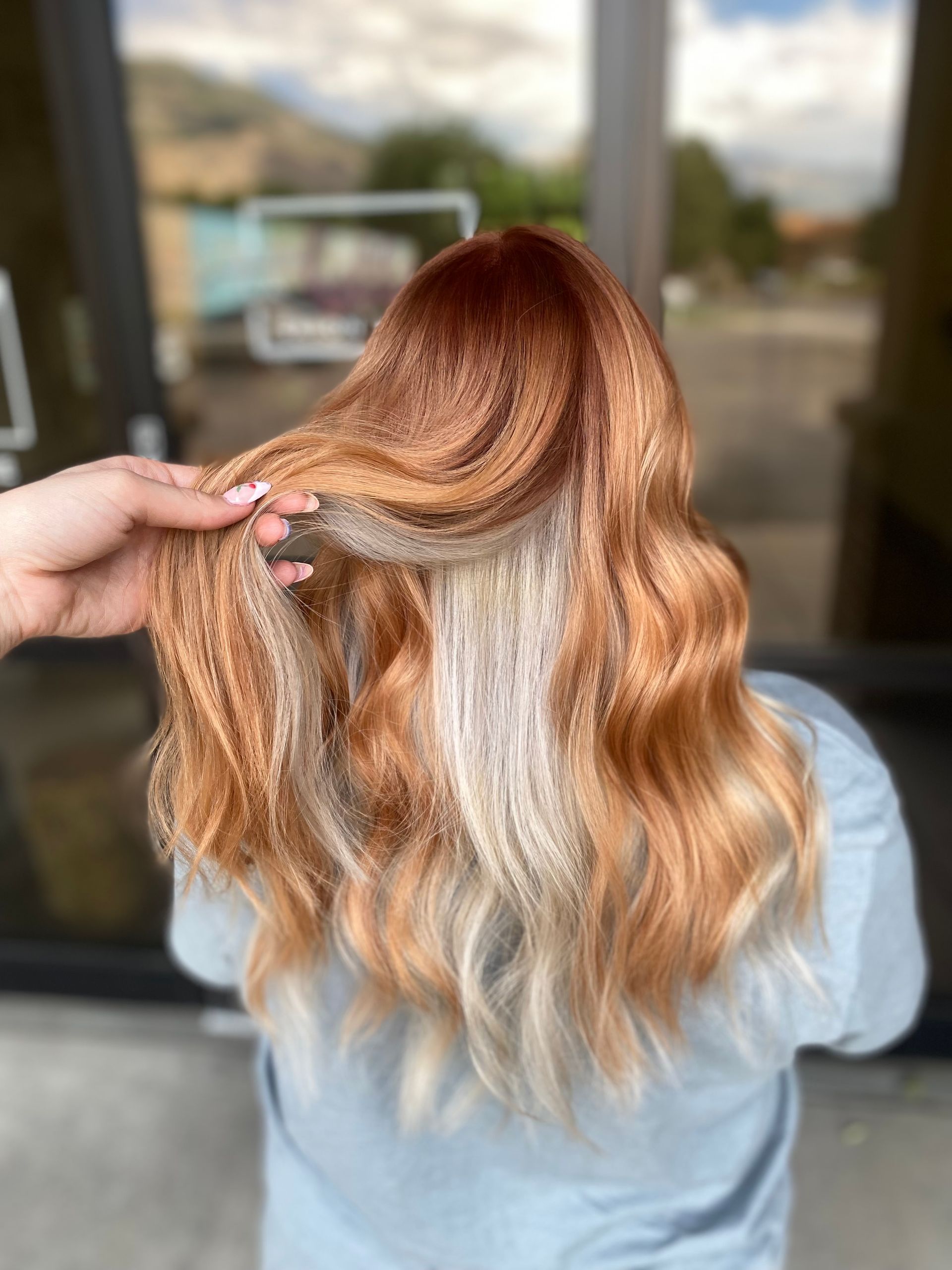 Person with long wavy hair, red-orange with blonde ombre, being held by hand.