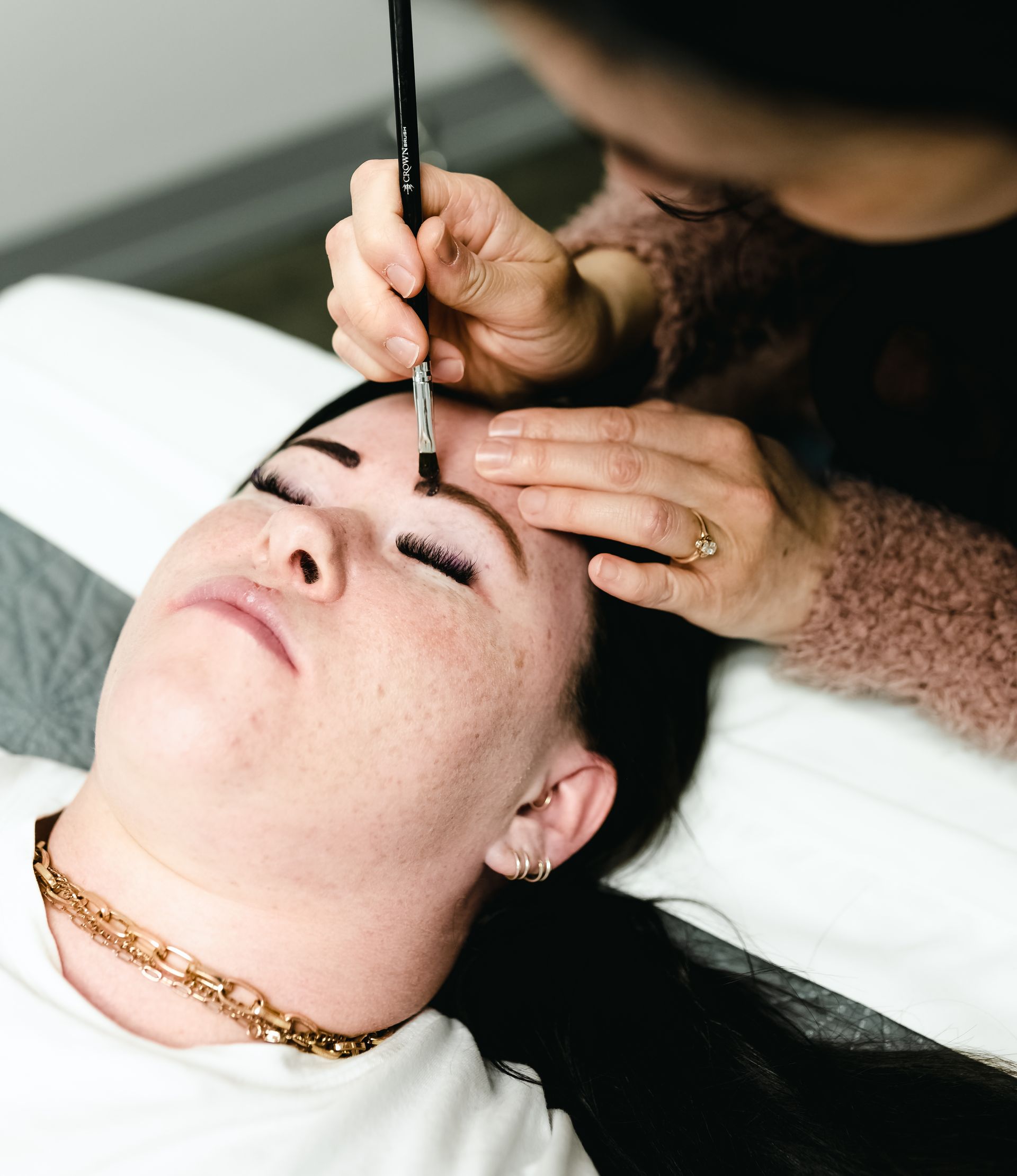 Woman getting eyebrow makeup applied with a brush, in a salon setting.