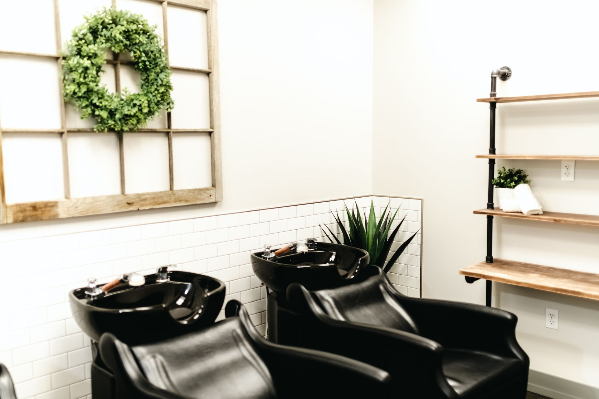 Hair salon with black sinks, chairs, and a wooden shelf with plants.