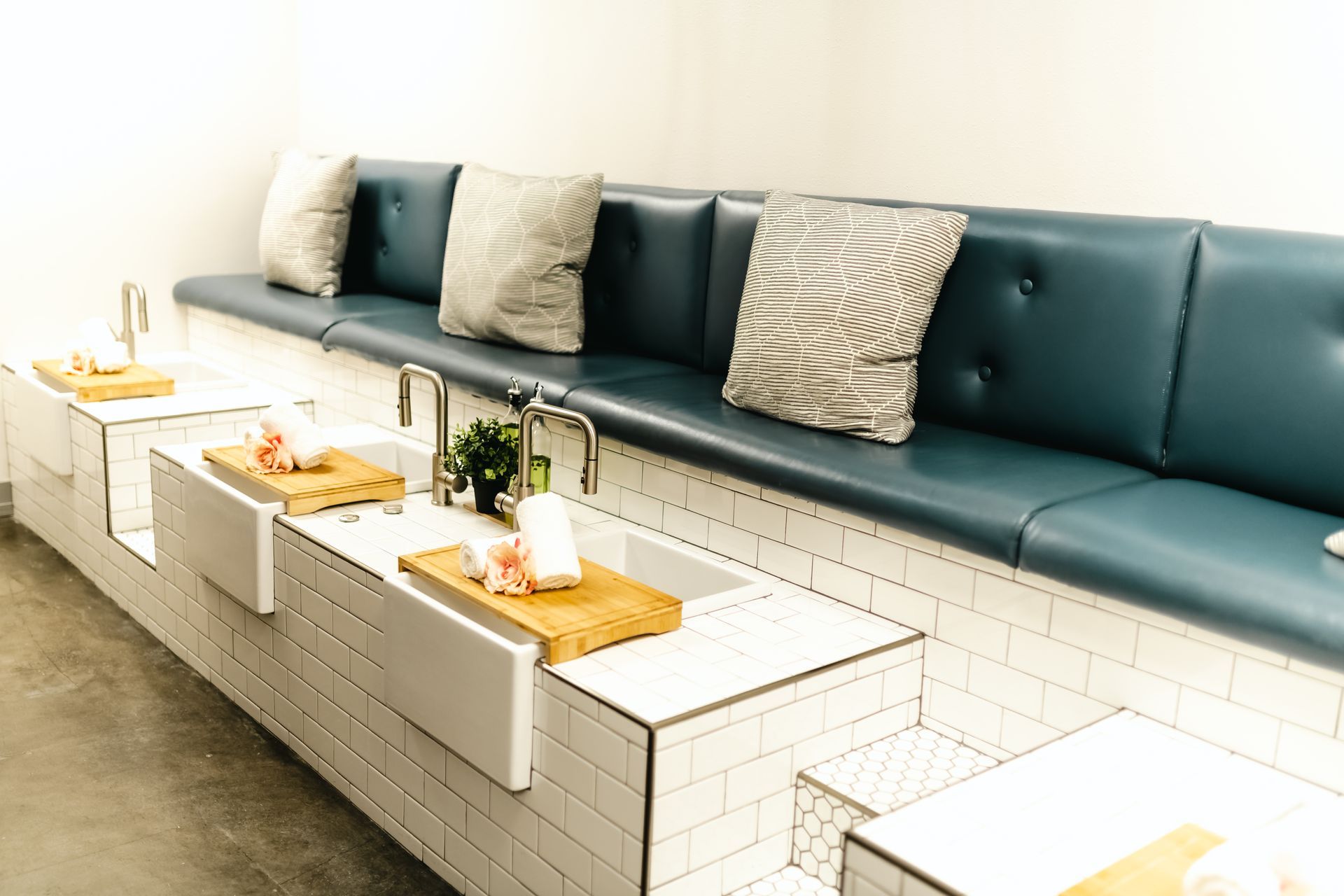 Pedicure station with blue bench, white tile, sinks, pillows, and wood trays.
