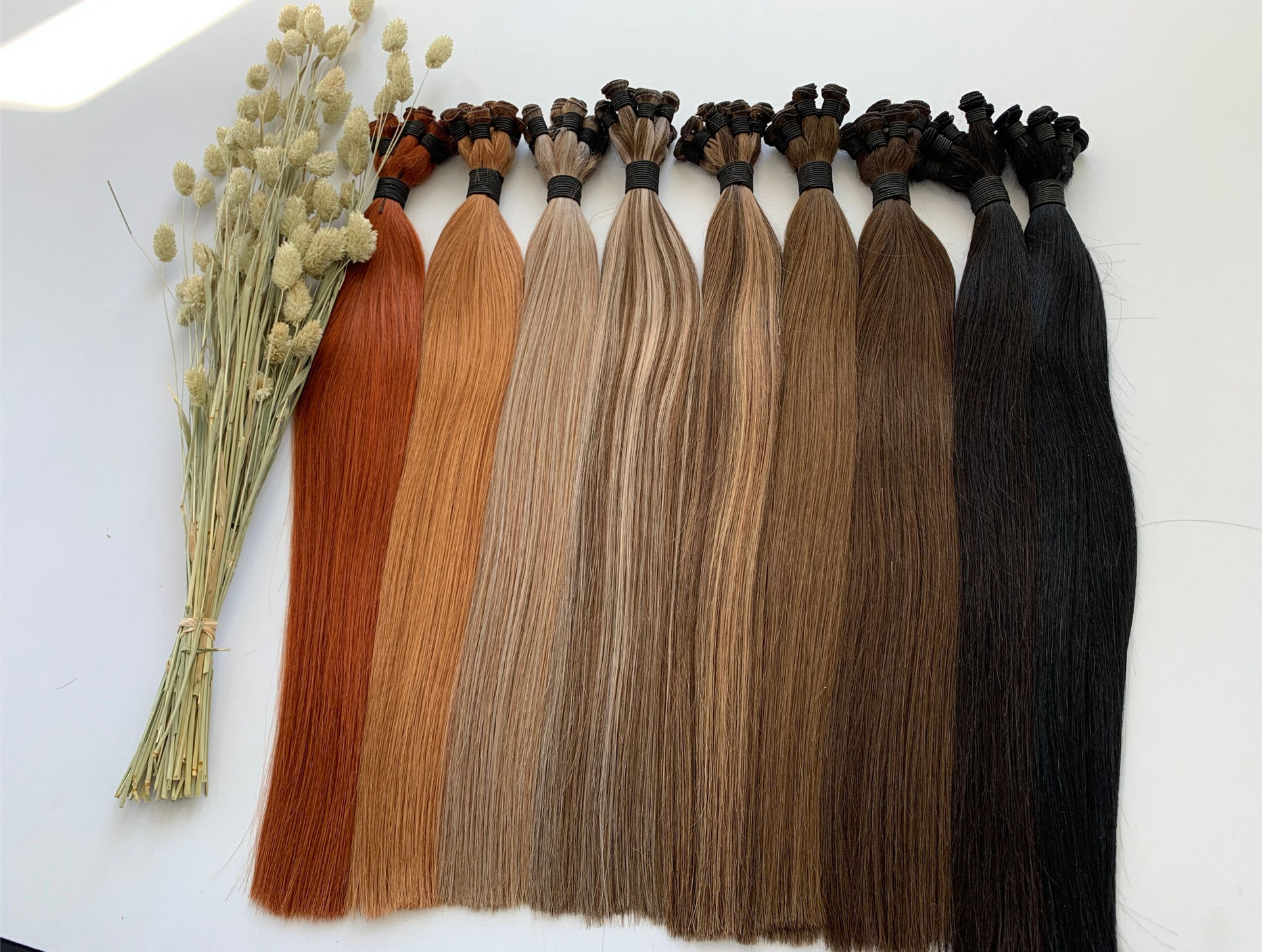 Bundles of hair extensions in various brown shades, with dried flowers to the left.