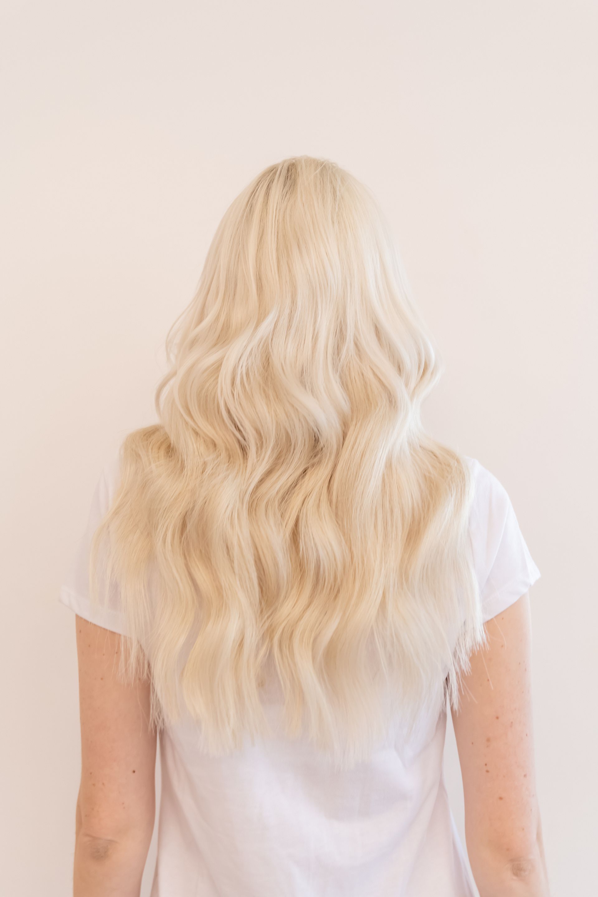Blonde woman with wavy, crimped hair, wearing a white shirt, facing away.