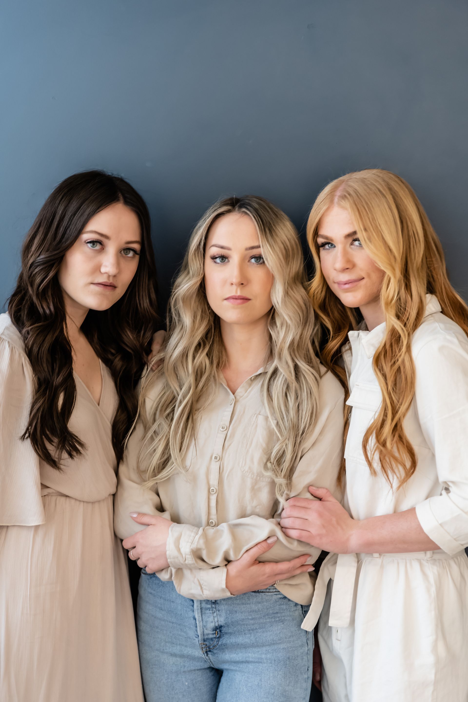 Three women are standing next to each other in front of a blue wall.