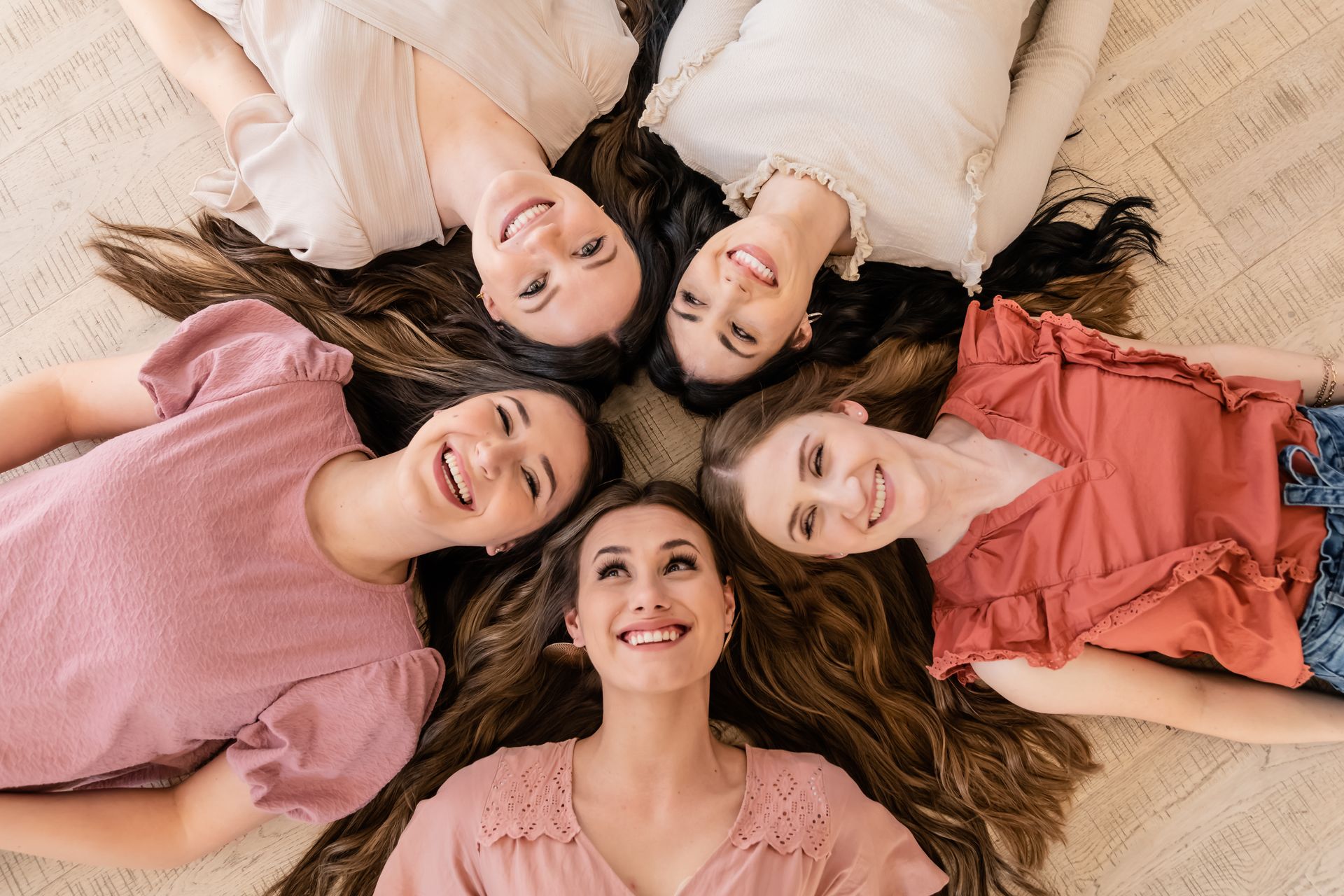 A group of young women are laying in a circle on the floor.