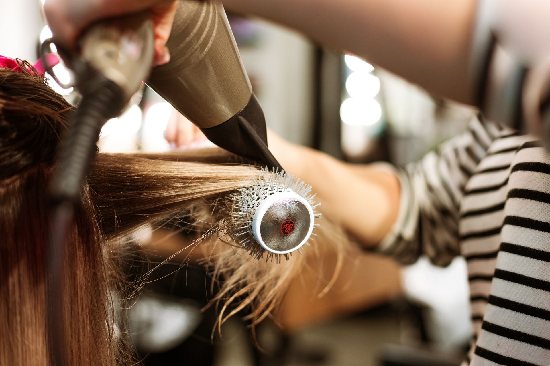 Close up to a hairstylist using a brush and hairdryer on a blond customer.