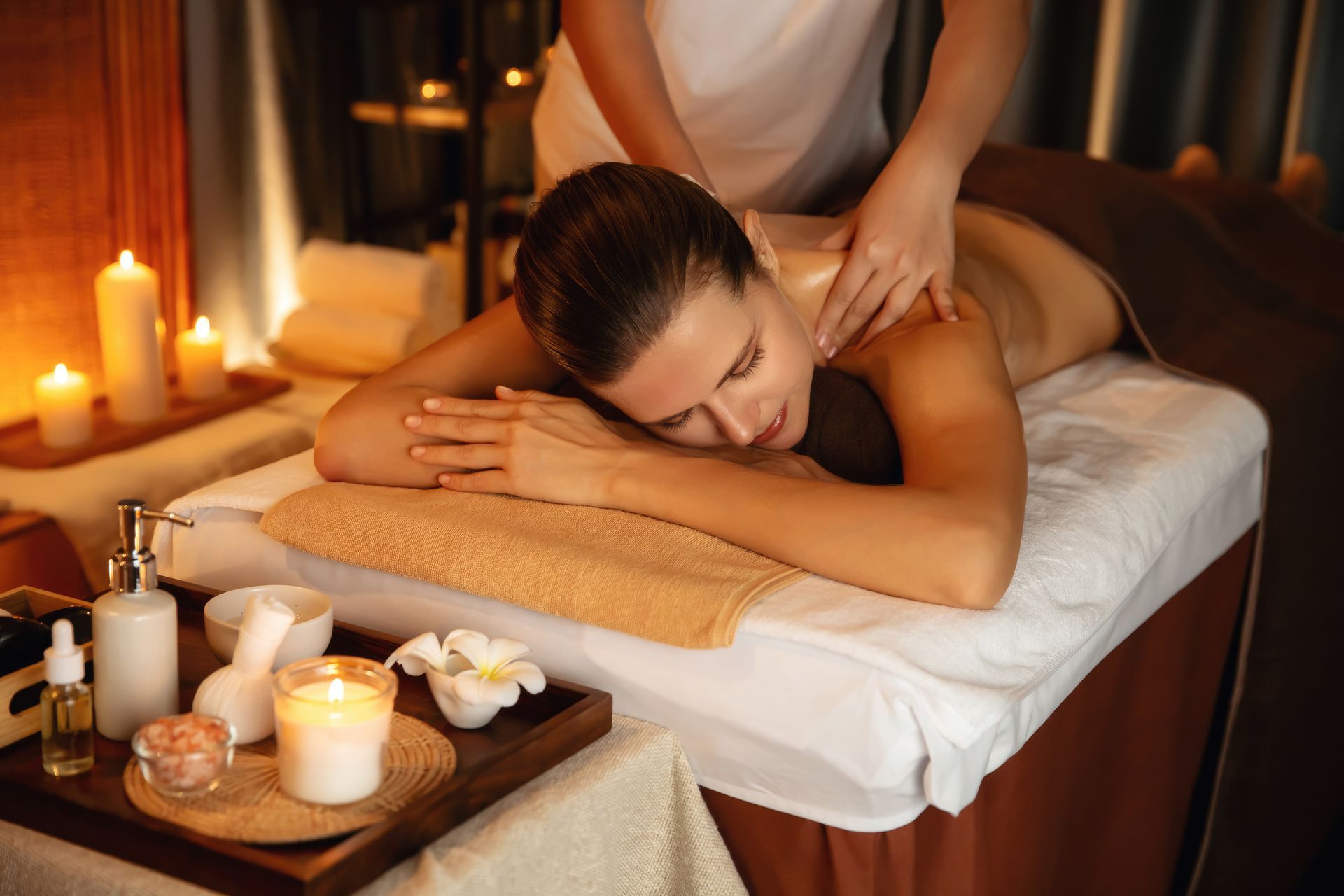 Woman relaxing on massage table with candles during luxury massage spa services.