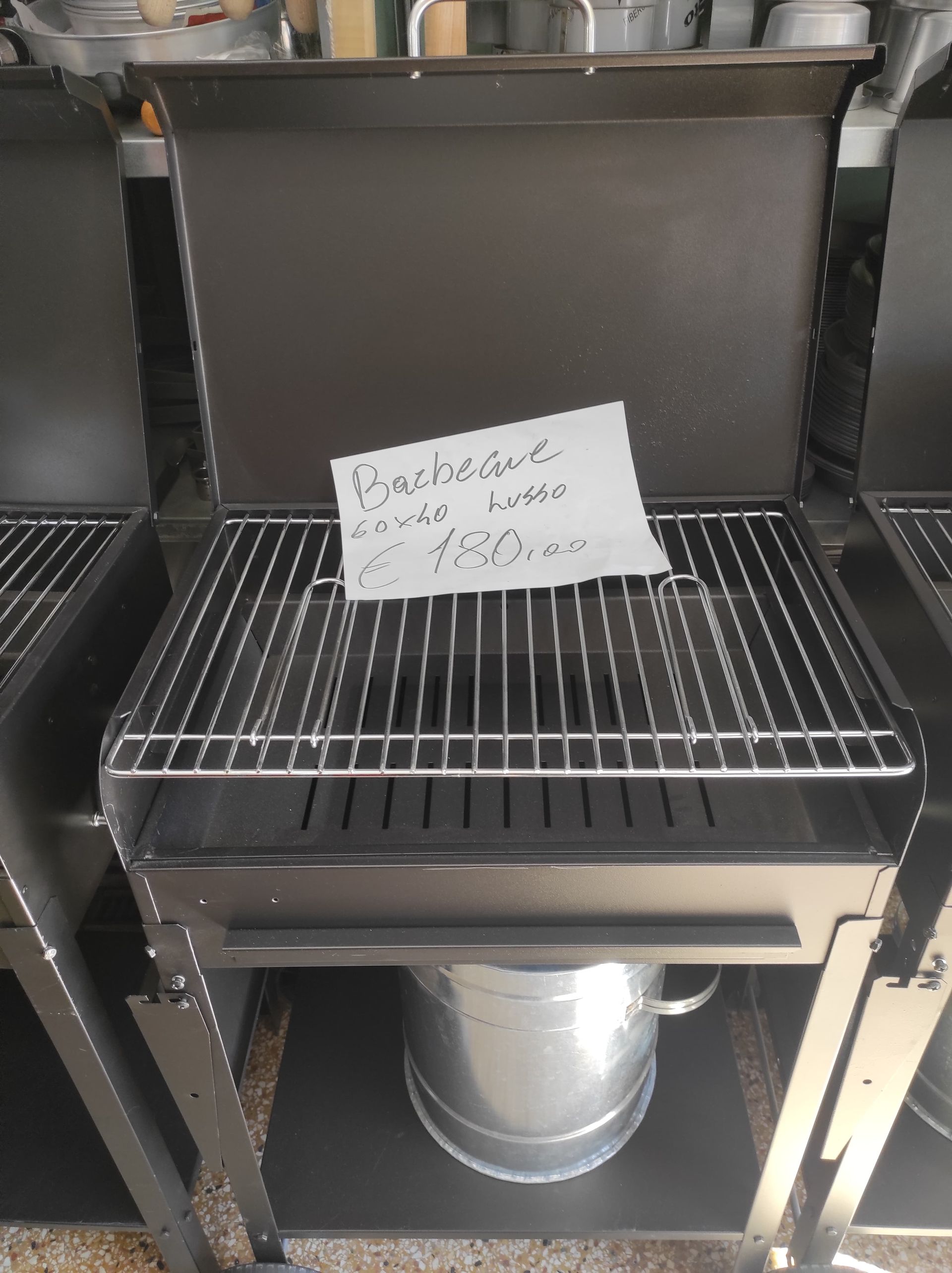 Griglia per barbecue in metallo nero con coperchio, griglia metallica e secchio metallico sottostante. Etichetta con il prezzo sulla griglia.