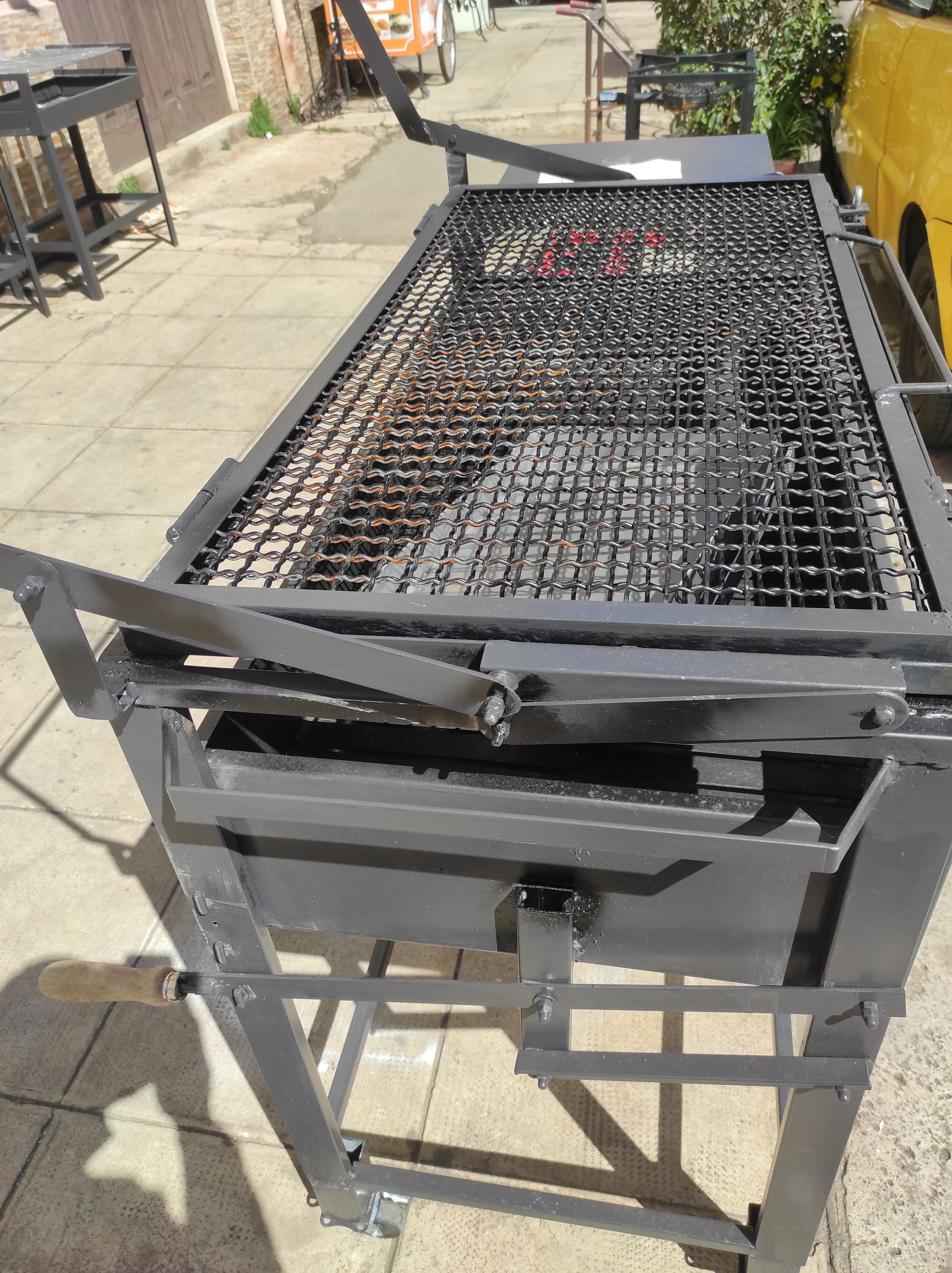 Grande barbecue da esterno in metallo grigio con griglia rialzata, posizionato su una superficie pavimentata.