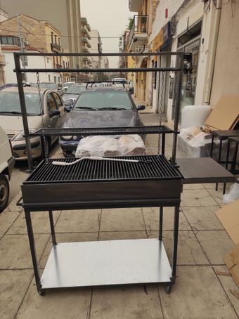 Barbecue in metallo all'aperto su un marciapiede cittadino, con una strada fiancheggiata da automobili sullo sfondo.