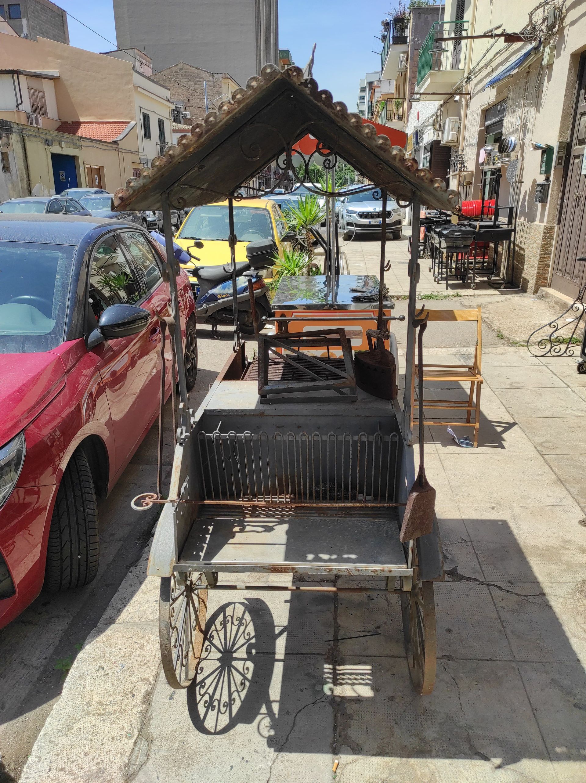 Un carretto del cibo consumato dal tempo con un piccolo tetto su una strada cittadina, un'auto rossa sulla sinistra.