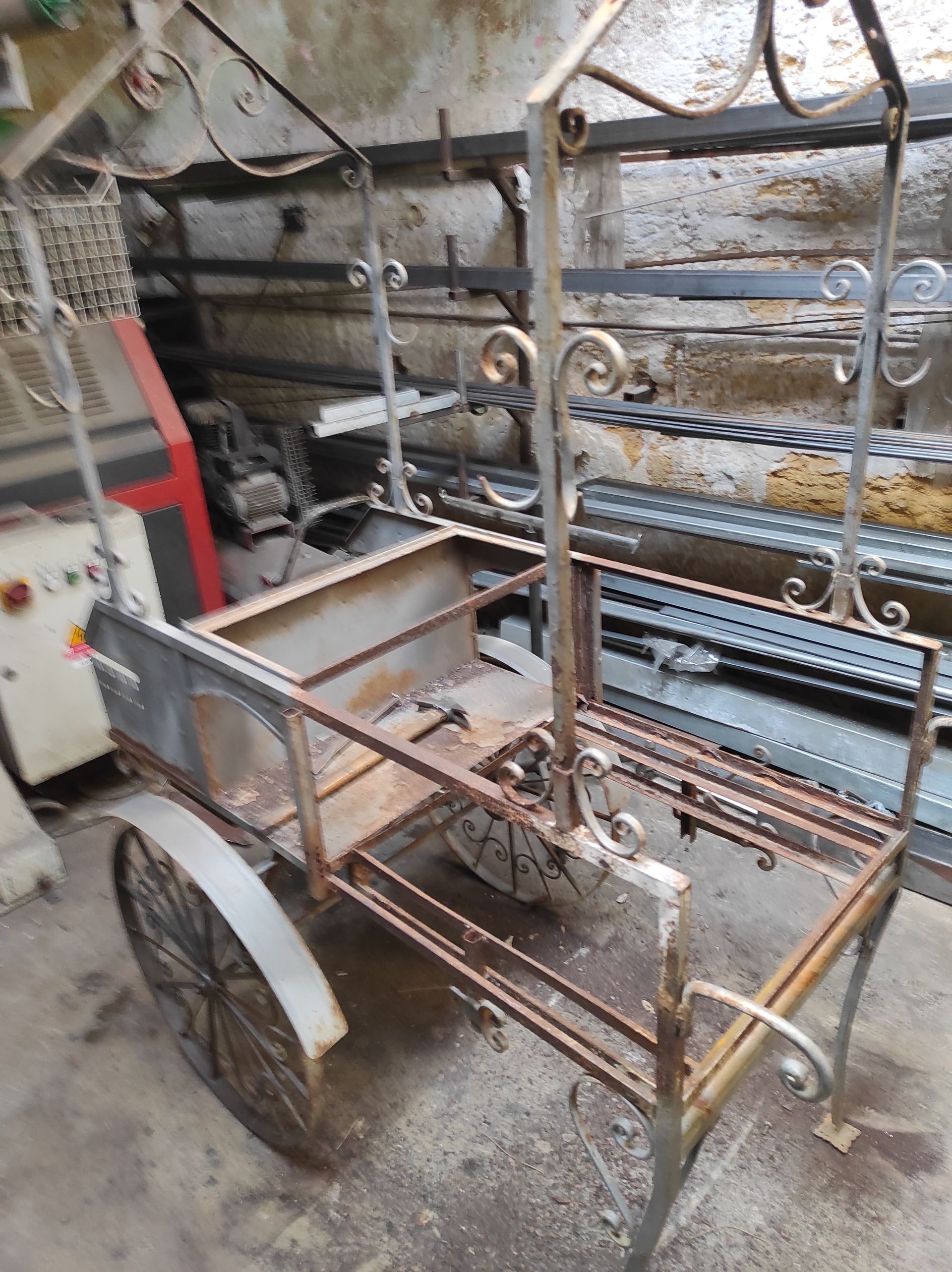 Carrello in metallo arrugginito con decorazioni, due ruote, ambientato in un'officina.