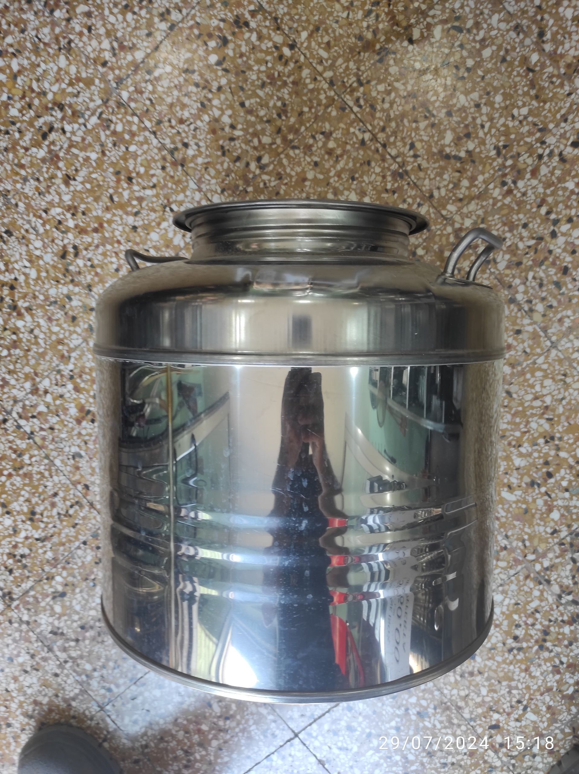 Contenitore in acciaio inossidabile lucido con manico su superficie maculata.