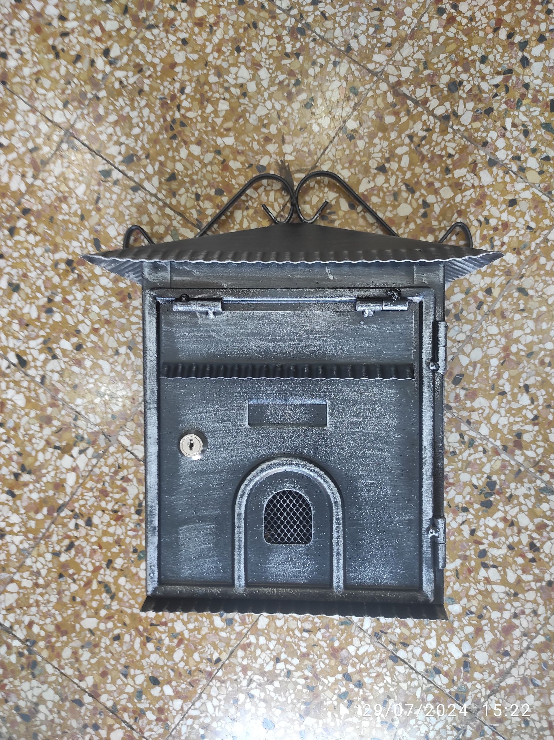 Cassetta postale in metallo nero con parte superiore decorata e apertura ad arco.