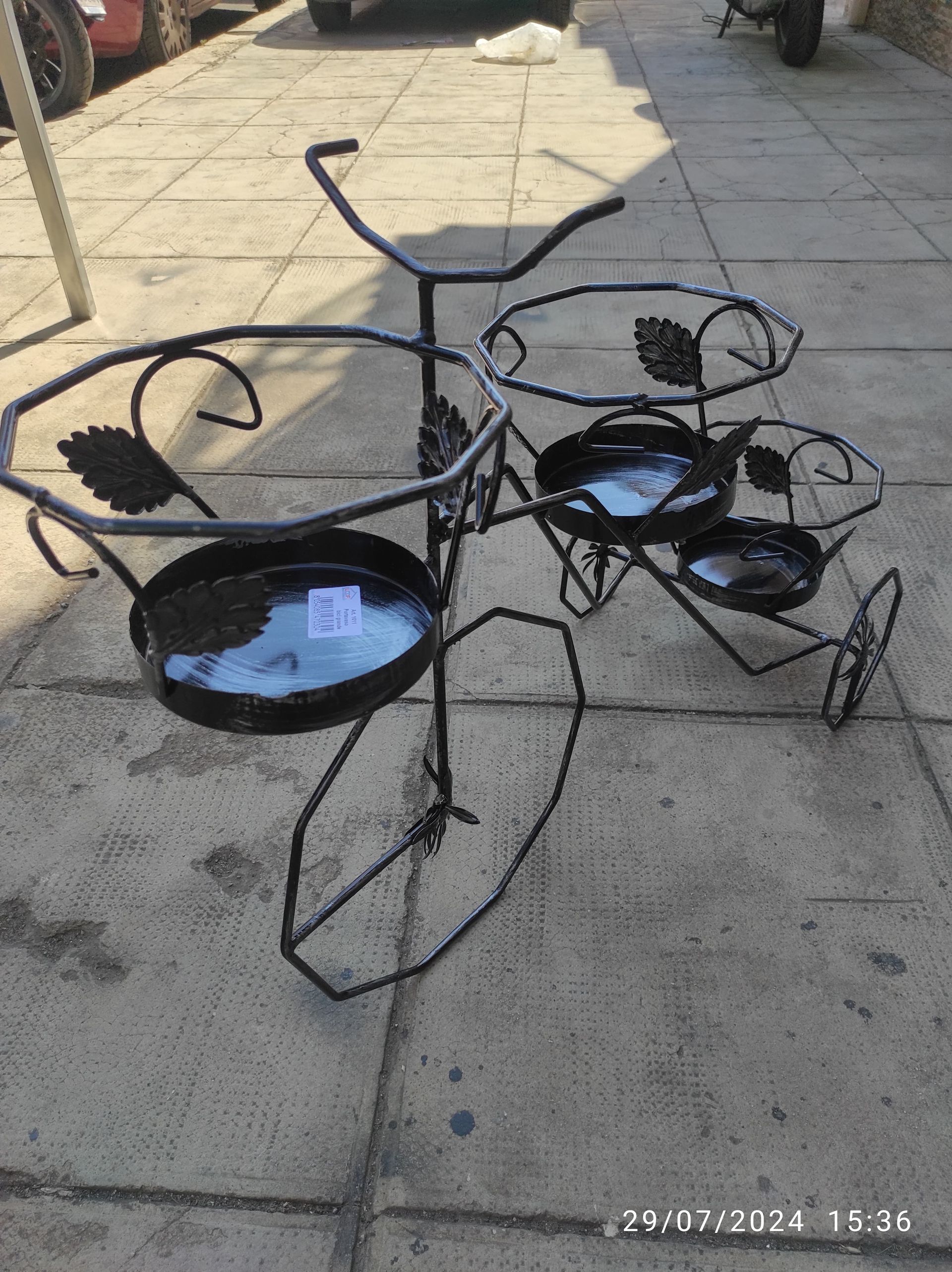 Supporto decorativo in metallo nero a forma di bicicletta con quattro supporti, su un marciapiede.