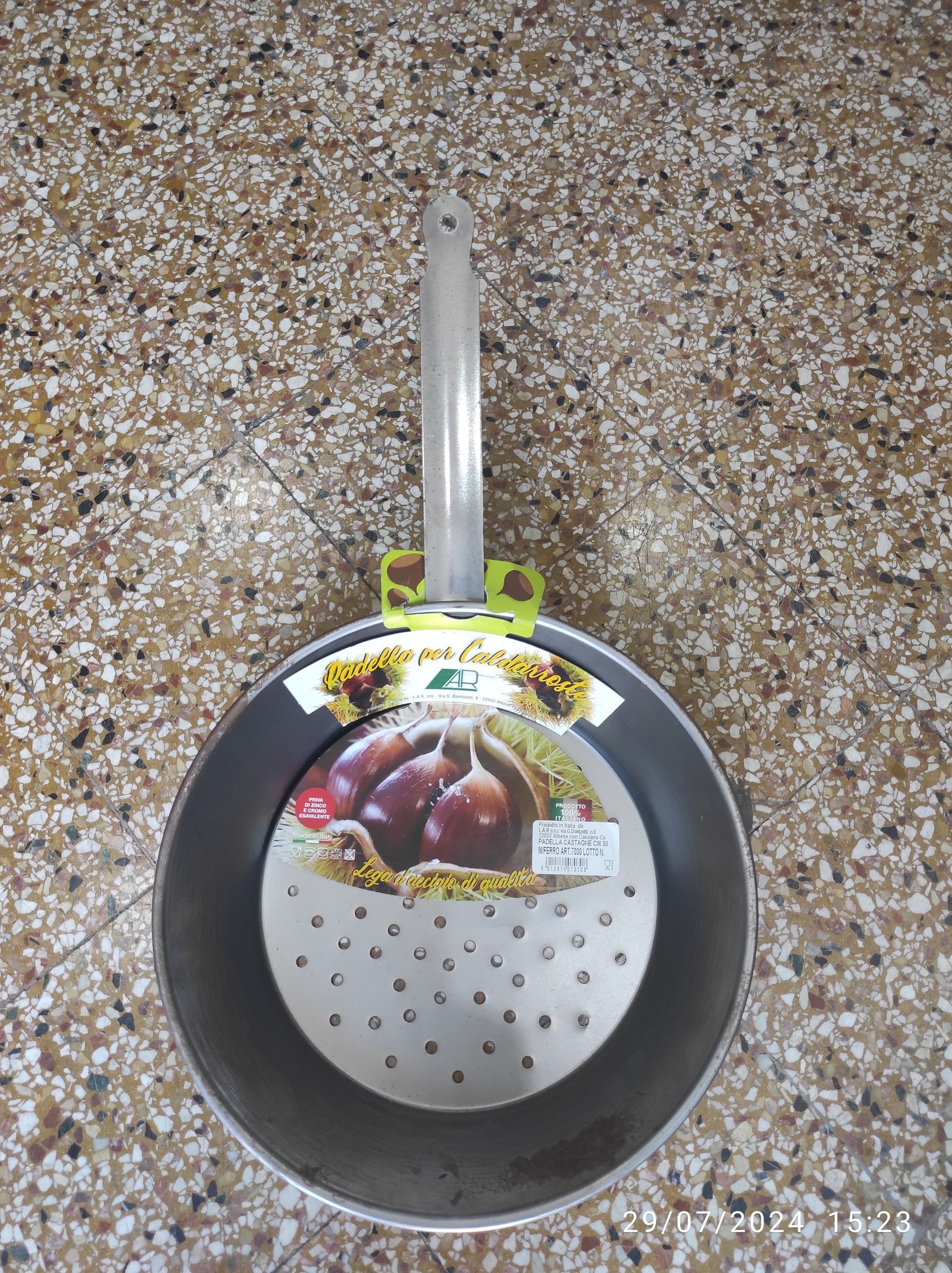 Padella con manico lungo, interno grigio ed etichetta del prodotto su superficie decorata.