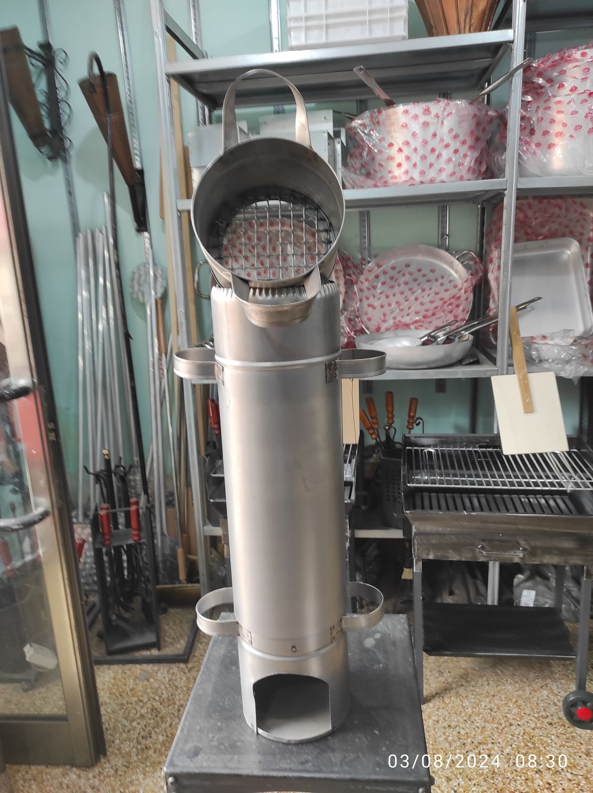 Una stufa a razzo in acciaio inossidabile con griglia aperta sulla parte superiore, in un'officina.