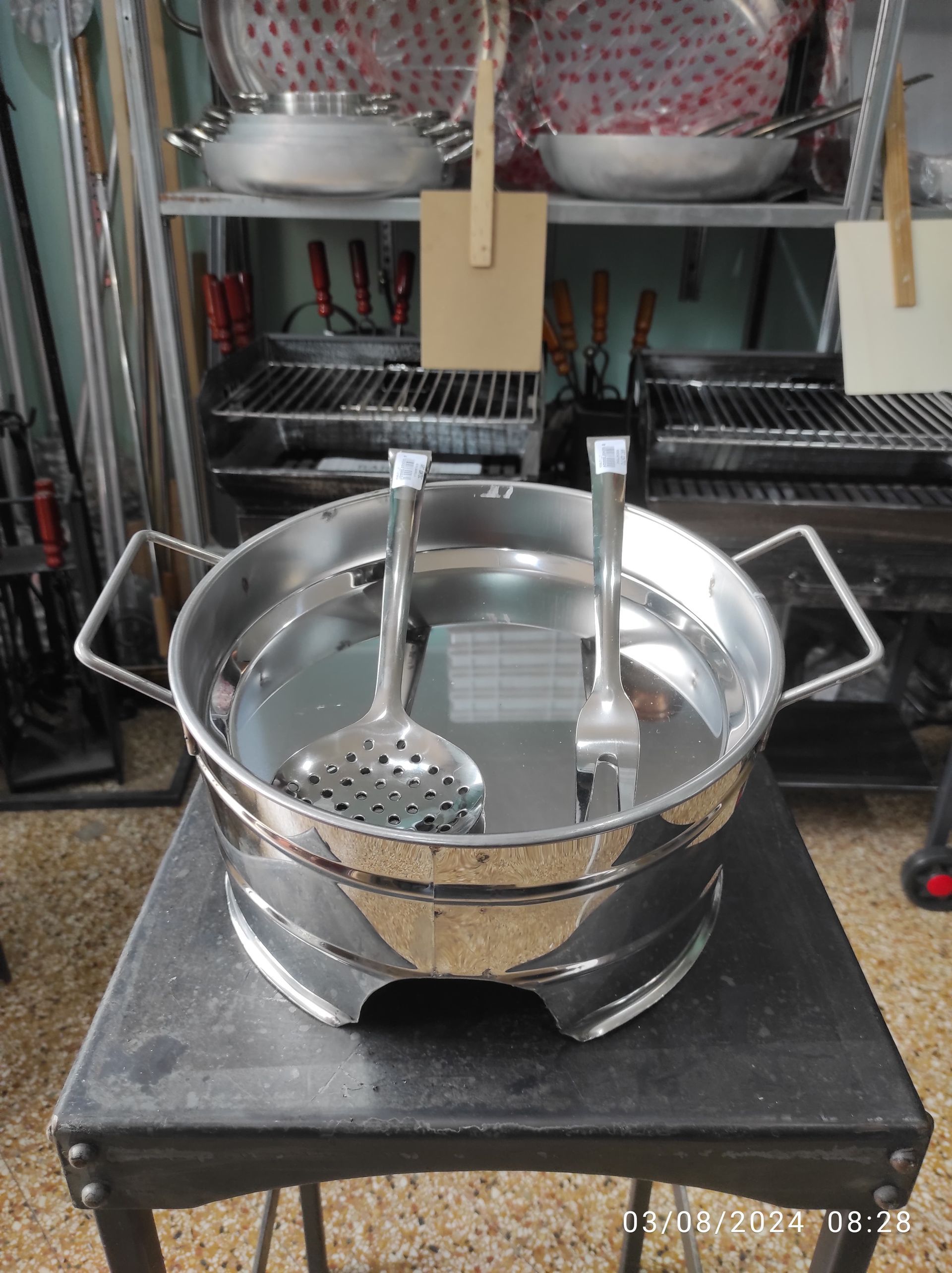 Pentola in acciaio inossidabile con schiumarola e forchetta su un tavolo nero, cucina.