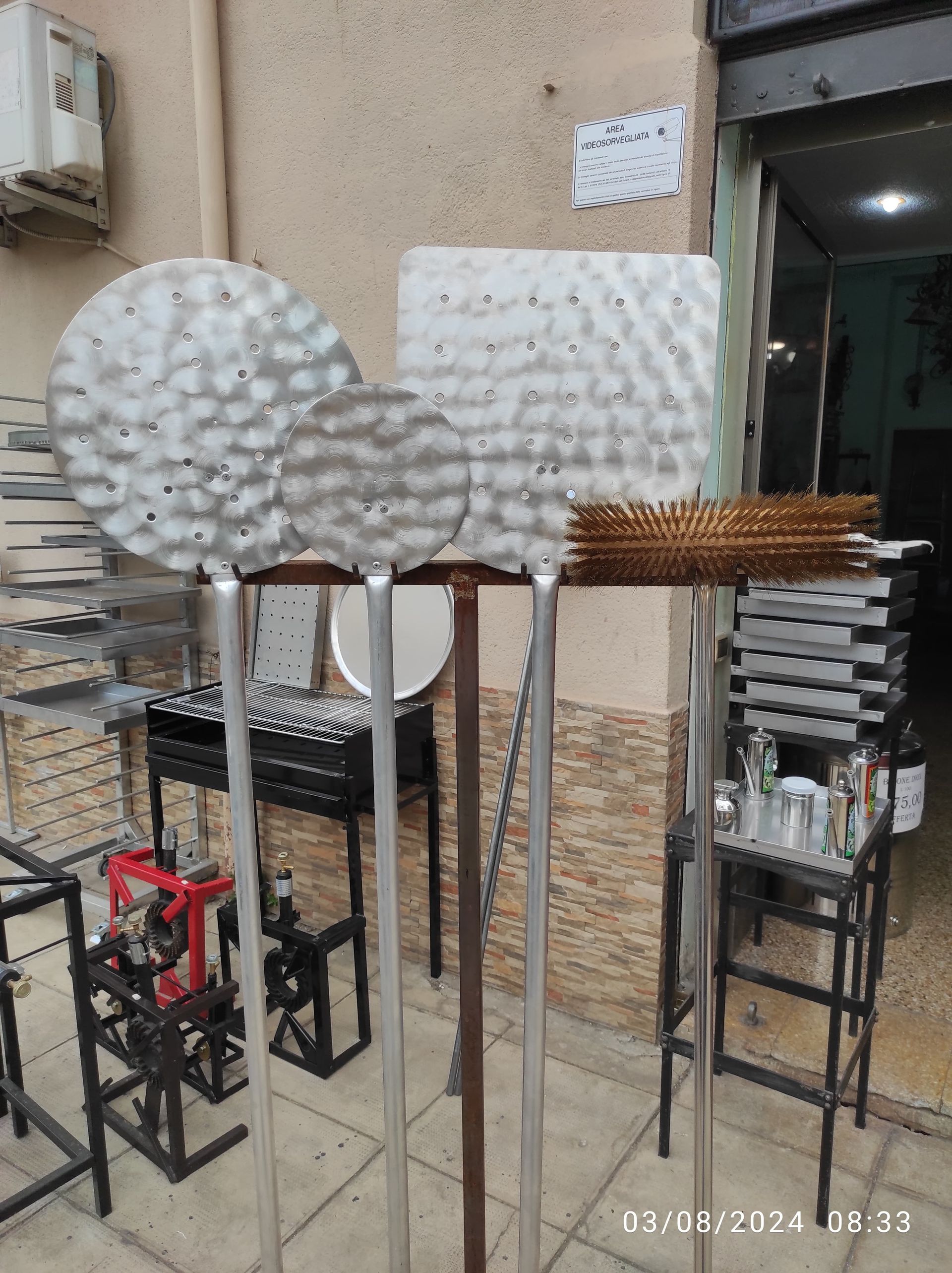Pale per pizza in metallo e accessori per griglia esposti fuori da un negozio.