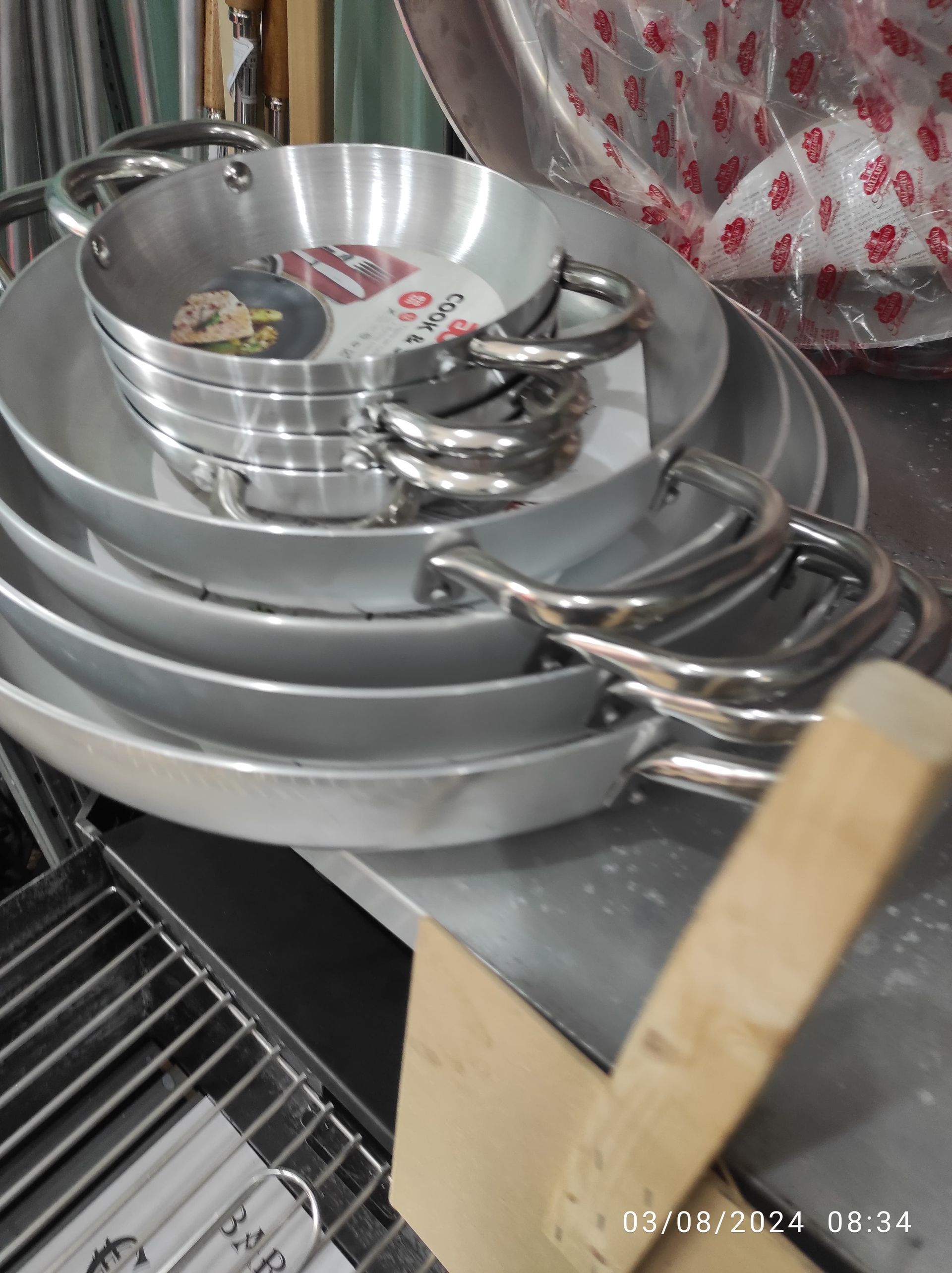 Pila di padelle d'argento con manici ad anello, impilate su una superficie metallica.