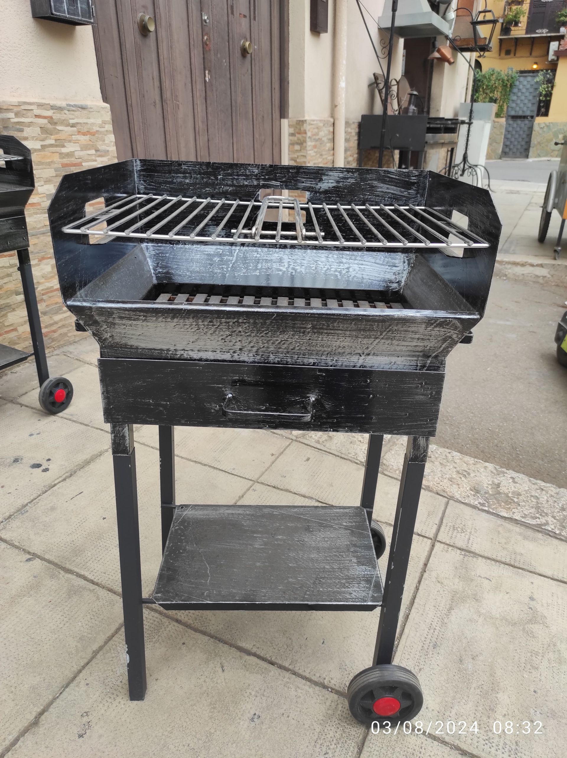 Barbecue a carbone nero da esterno su un patio, con griglia in metallo e ruote.