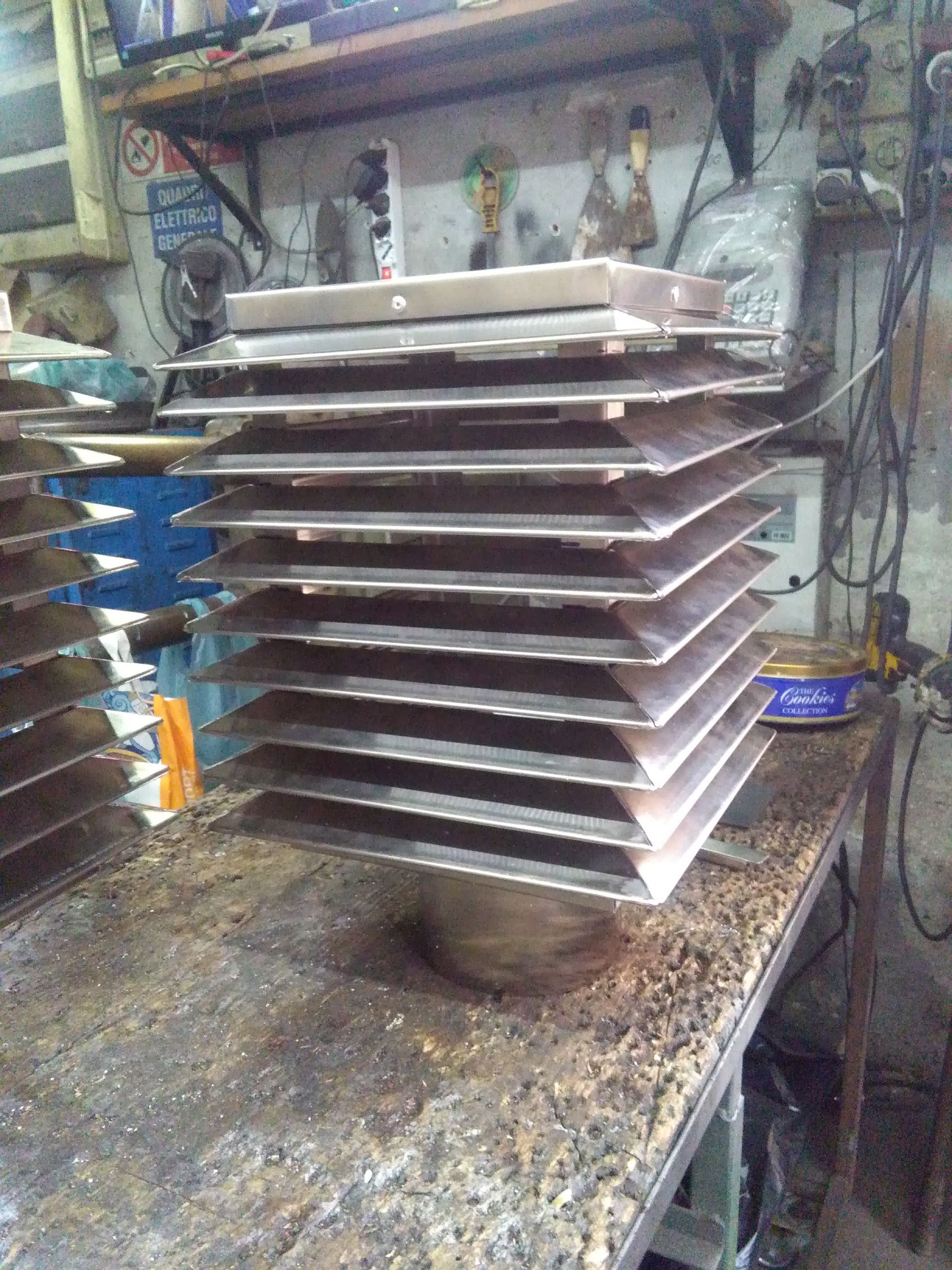 Pila di vassoi di metallo su un banco da lavoro disordinato in un'officina.